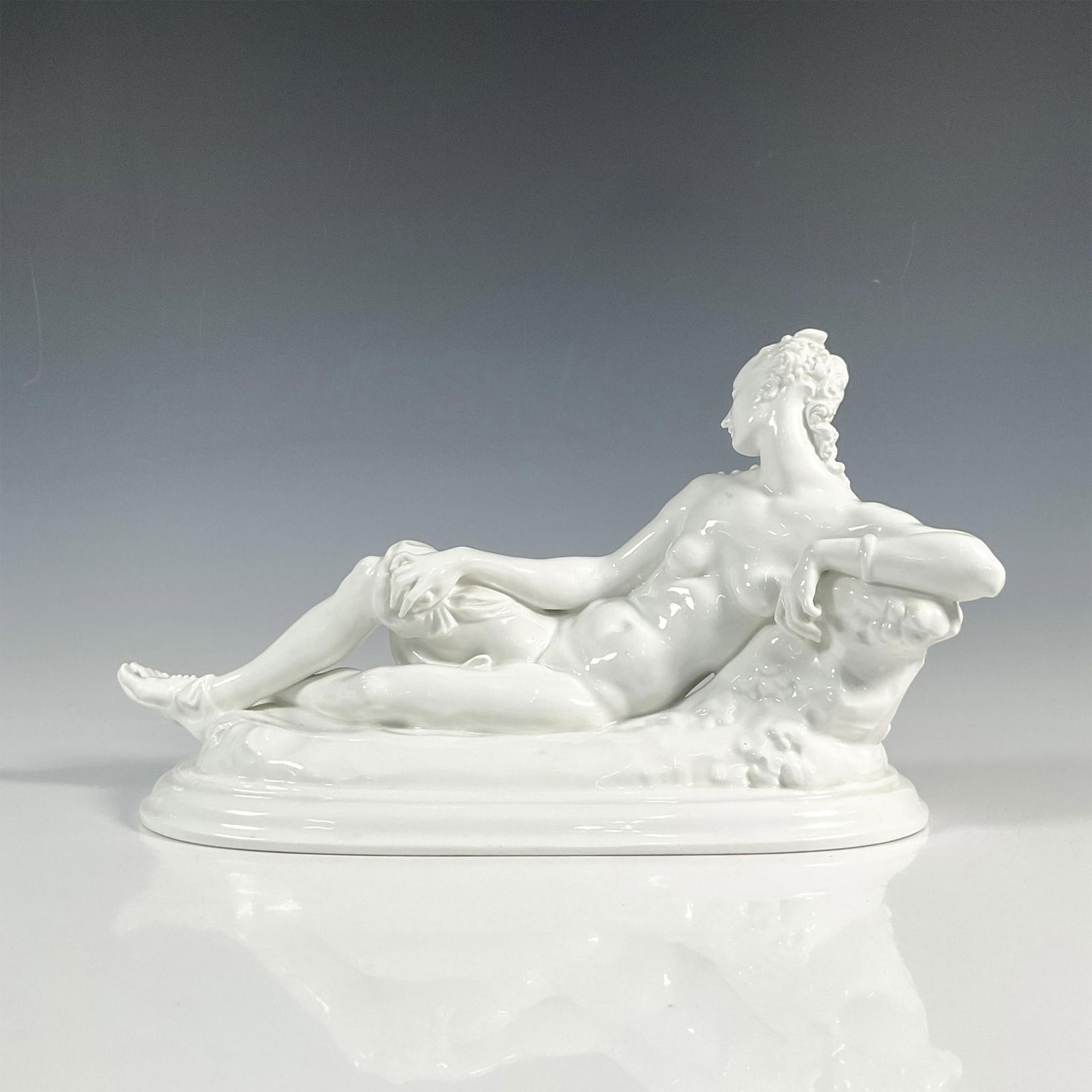 KPM Berlin Paul Scheurich Porcelain Figure, Ruhende: White porcelain figure of a reclining female nude with cloth on naturalistic pedestal over oval base. KPM scepter mark to underside. Artist: Paul Scheurich Issued: 1917 Dimensions: 15.5"L x 7"W x 9.5"