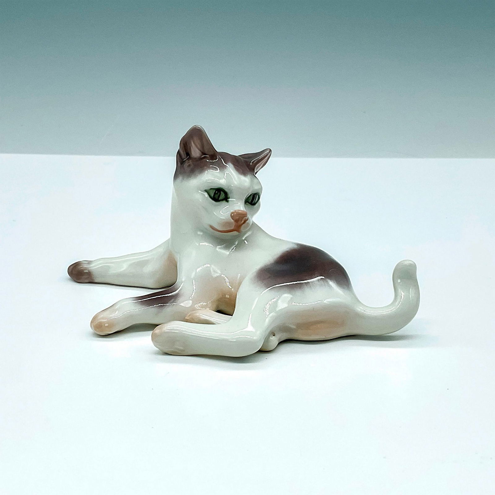 DJ Copenhagen Porcelain Figurine, Reclining Cat 1006: Dahl Jensen porcelain cat in grey and white. DJ Copenhagen backstamp. Issued: 20th Century Dimensions: 5.5"L x 3"W x 2.5"H Manufacturer: Dahl Jensen DJ Copenhagen Country of Origin: Denmark