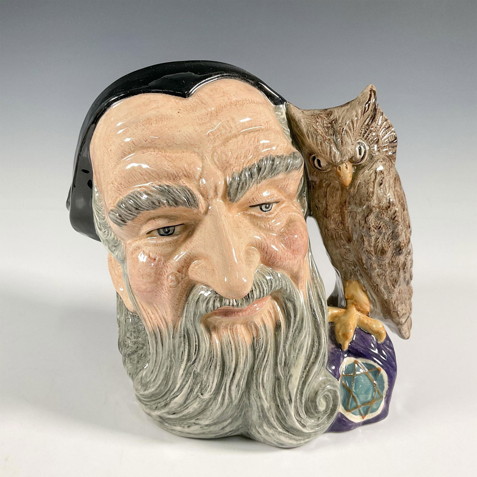 Merlin D6529 - Large - Royal Doulton Character Jug: Part of the Characters From Literature series. Black, grey, and brown coloration with owl handle. Royal Doulton backstamp. Artist: Garry Sharpe Issued: 1960-1998 Dimensions: 8"L x 6"W x 7.75"H Manufac