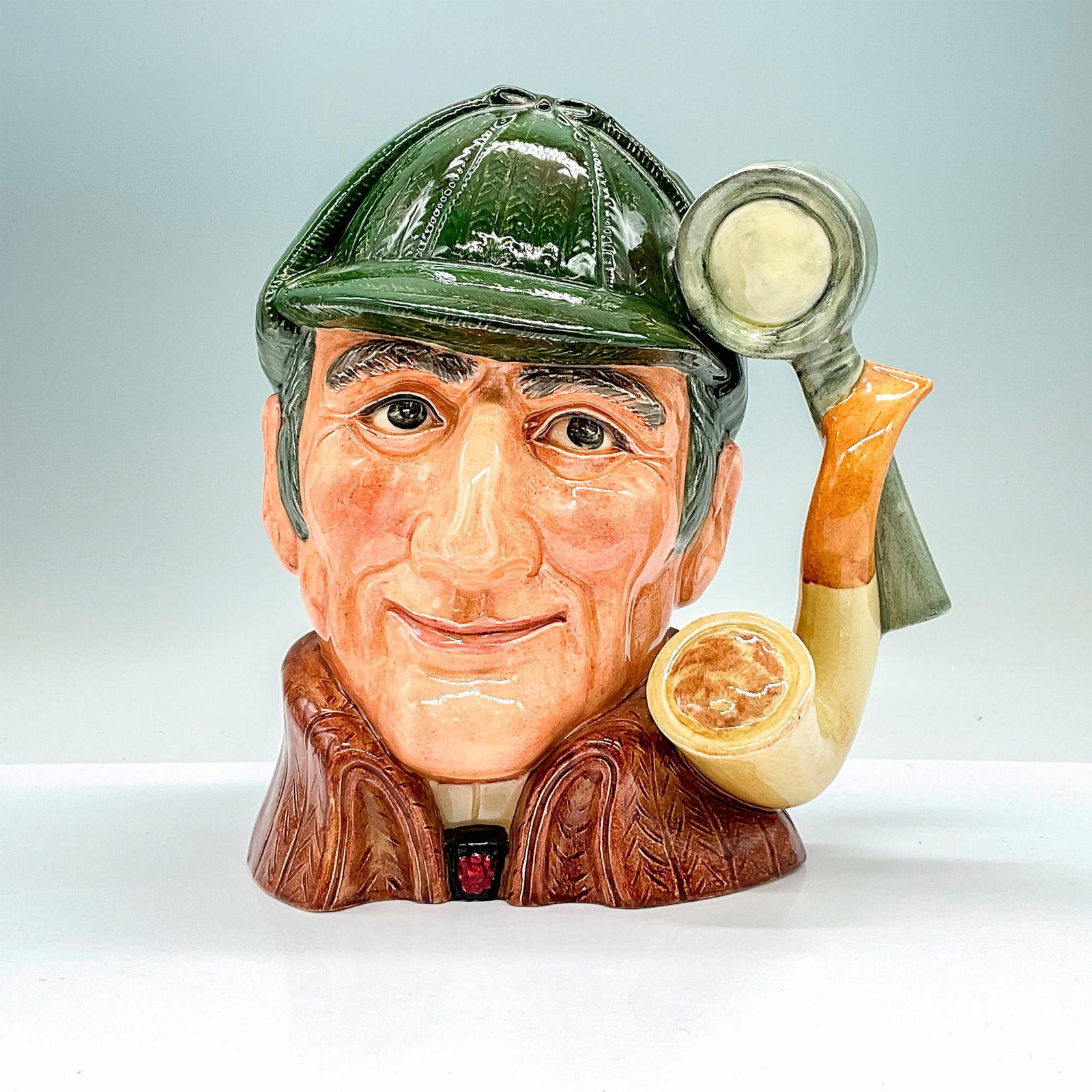 Sleuth D6631 - Large - Royal Doulton Character Jug: Variation One. Dark green deerstalker hat, brown cloak. Royal Doulton backstamp. Artist: Alan Moore Issued: 1973 - 1996 Dimensions: 7"H Manufacturer: Royal Doulton Country of Origin: England
