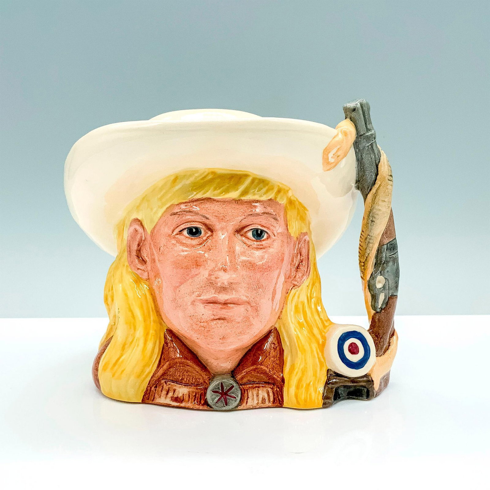 Annie Oakley D6732 - Odd Size - Royal Doulton Character Jug: Yellow hair; cream hat; brown tunic. Royal Doulton backstamp. Artist: Stanley J. Taylor Issued: 1985 - 1989 Dimensions: 5.25"H Manufacturer: Royal Doulton Country of Origin: England