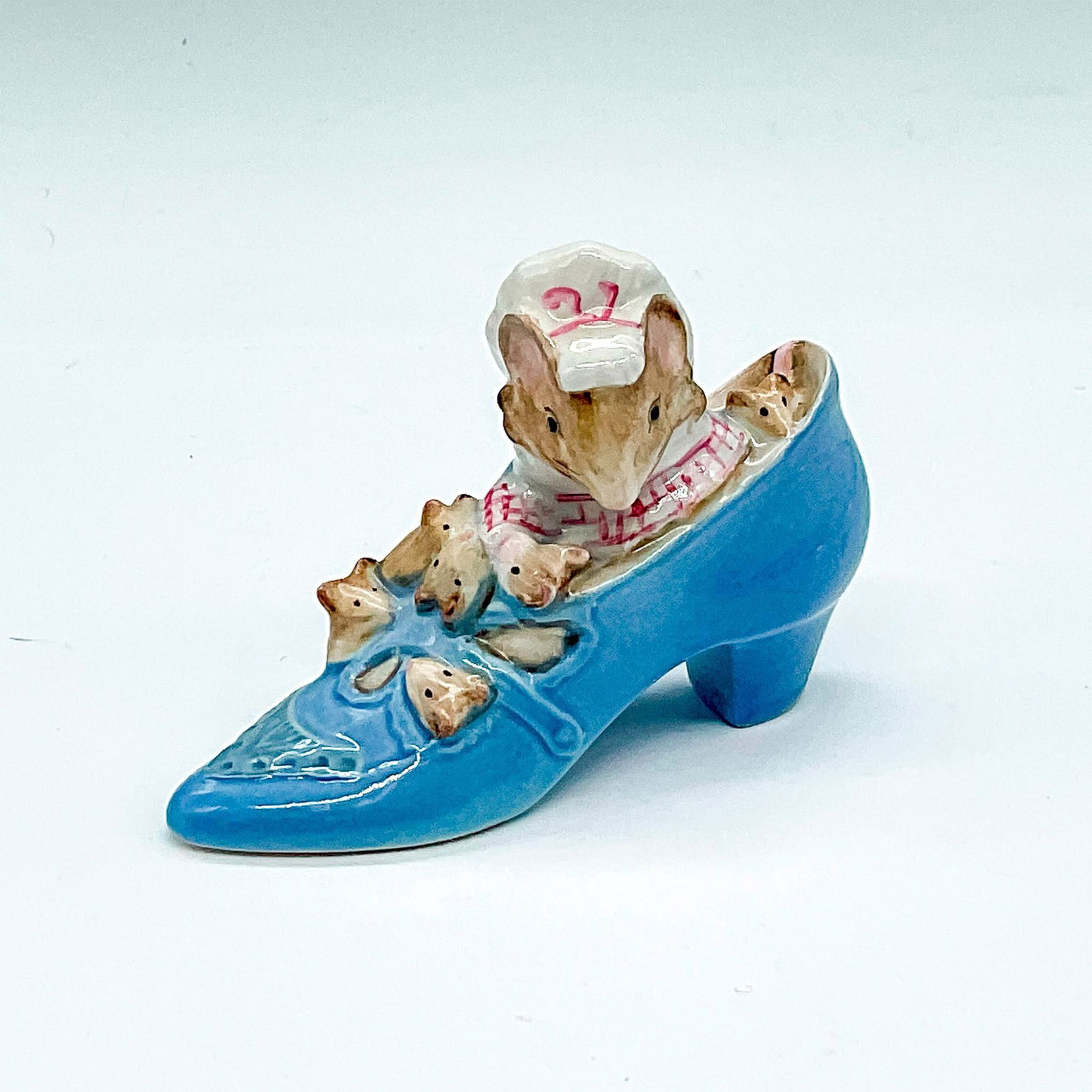 Beswick Beatrix Potter's Figurine, Mouse in Shoe: The Old Woman Who Lived In A Shoe, figurine in white dress and bonnet with pink accents, living in a sky-blue shoe with her children. Beswick Gold Oval backstamp. Issued: 20th century Dimensions: 4"L