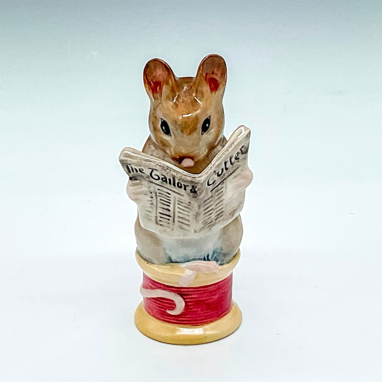 Beswick Beatrix Potter's Figurine, Tailor of Gloucester: Hand painted, reading a newspaper while sitting on top of a spool of magenta thread. Beswick Gold Oval backstamp. Issued: 20th century Dimensions: 1.25"L x 1.25"W x 3.5"H Manufacturer: Beatrix Potter