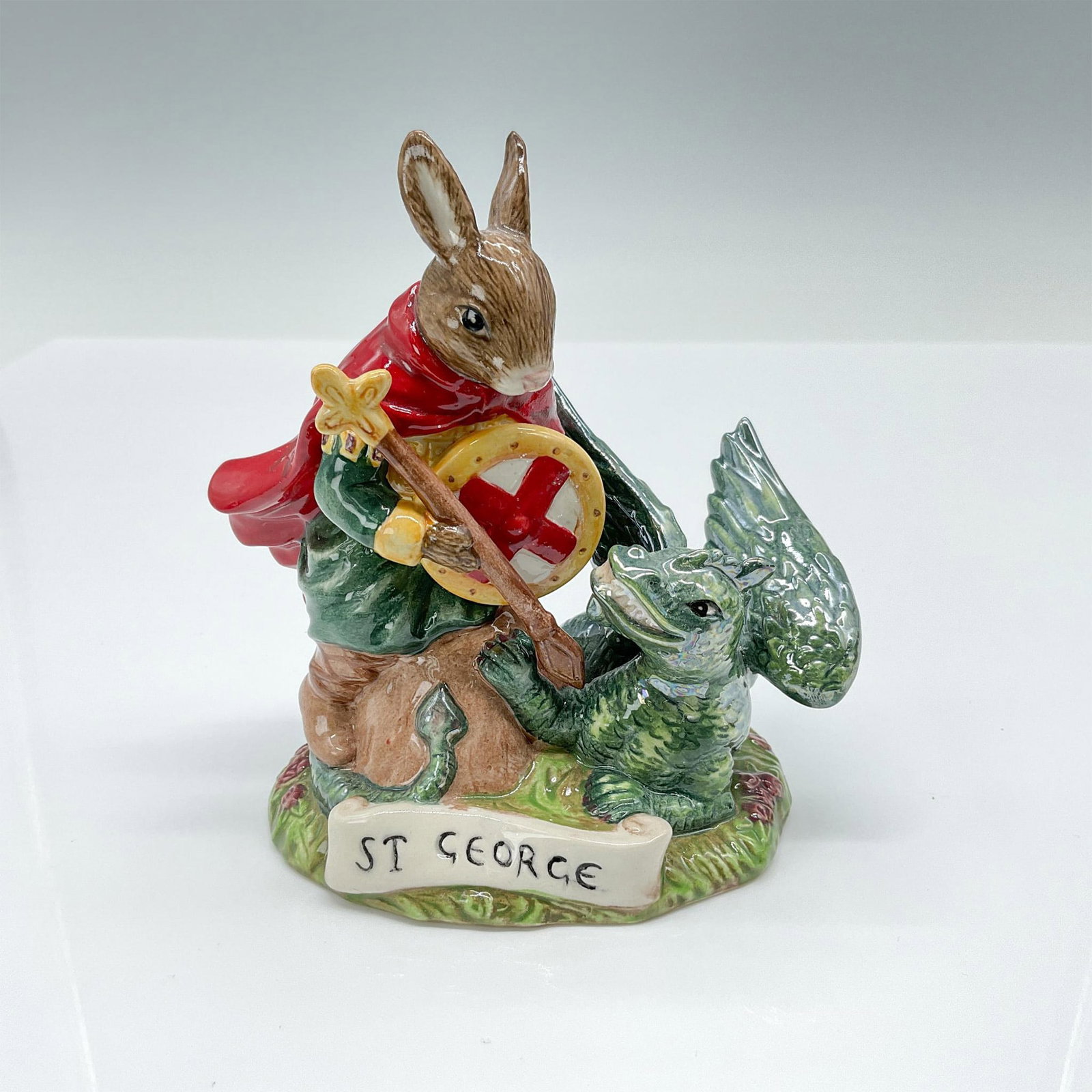 Saint George DB398 - Royal Doulton Bunnykins: This Bunnykins figurine depicts St. George, the patron saint of England, in the act of slaying a dragon, showcasing red and green sparkling coloration. Royal Doulton backstamp. Issued: 2005 Dimensions