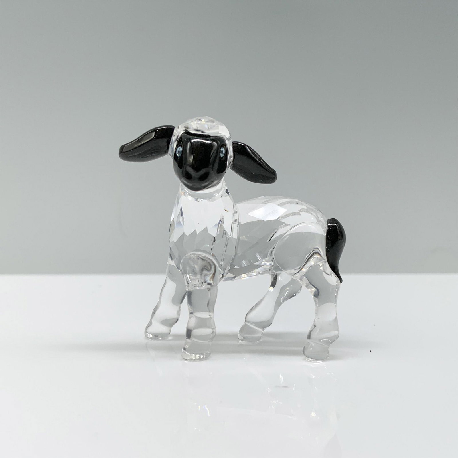 Swarovski Crystal Figurine, Little Black Face Lamb 654305: A clear crystal lamb standing on all fours with black crystal used for the face, ears, and tail. Swarovski backstamp. This item has its original box. Dimensions of the box: 2.25"H x 3.25" dia. Artist: