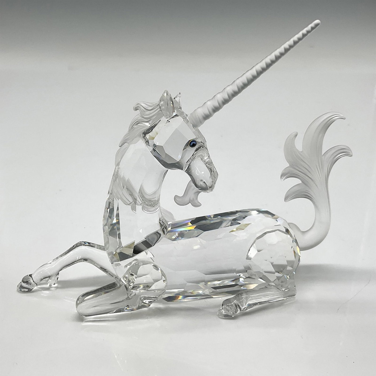 Swarovski SCS Crystal Figurine, 1996 Unicorn: First of the Fabulous Creatures trilogy. Seated clear faceted figural has satin crystal features of horn, whiskers, mane and tail with blue crystal eyes. Swarovski backstamp. 191727. This item has its