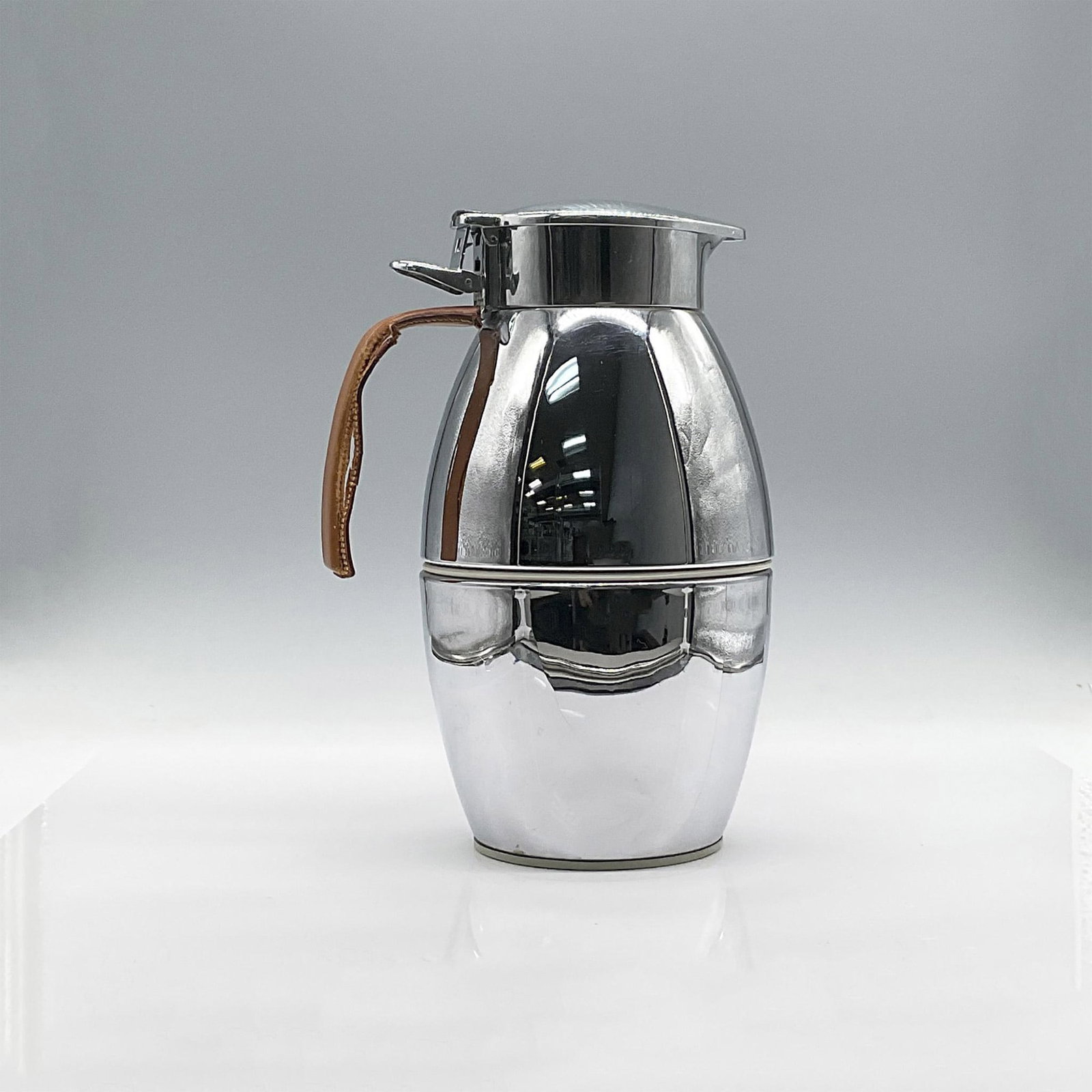 Hermes Chrome Insulated Carafe: Chromed steel barrel body with short cylindrical collar, integral spout and spring hinged lid. Rubber gasket and topper inside lid. Interior has double walled insulation. Curved single mount handle wi