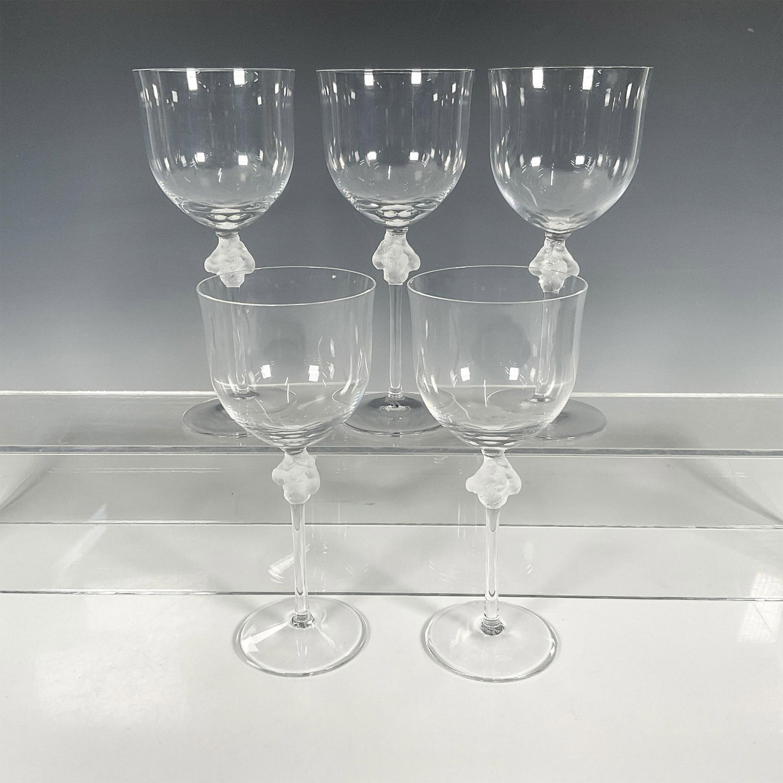 5pc Lalique Crystal Tall Water Goblets, Roxane: Five crystal water goblets with two nude women in frosted crystal on the stem. Pattern created by Marc Lalique in 1968. Lalique etched backstamp. Issued: 1968-2021 Dimensions: 3"W x 8.5"H Manufacturer