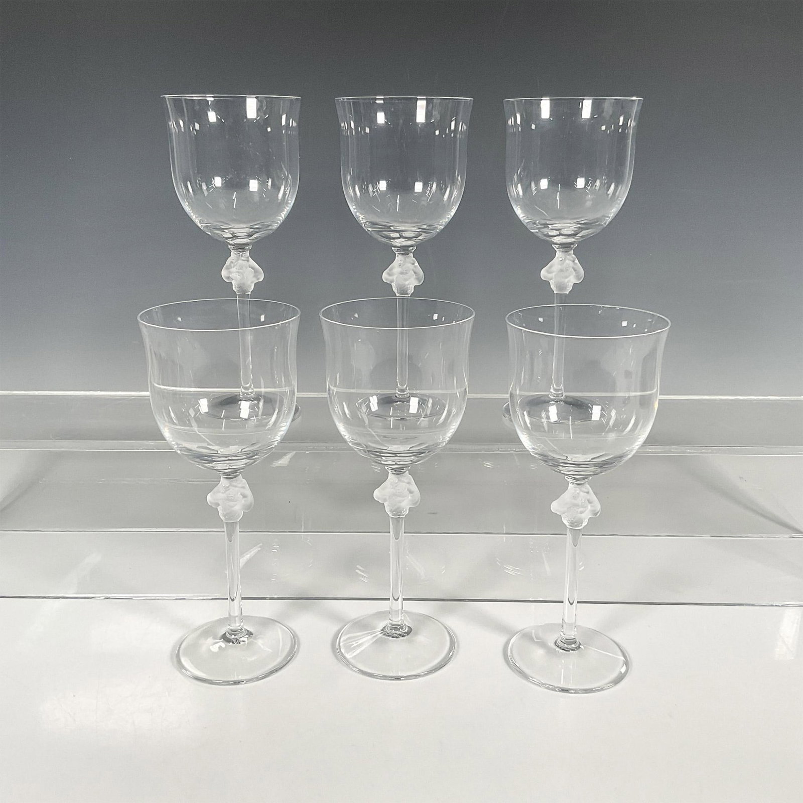6pc Lalique Crystal Burgundy Wine Glasses, Roxane: Six tall burgundy wine glasses with frosted piece atop of stem of two nude women in frosted crystal on the stem. Pattern created by Marc Lalique in 1968. Lalique etched backstamp. Dimensions: 2.75"W x