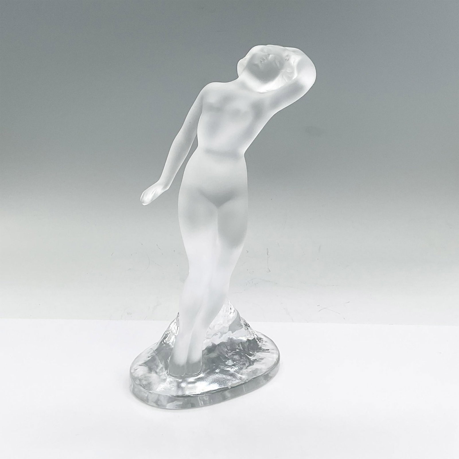 Lalique Crystal Figurine, Danseuse Bras Leves: Frosted crystal figure of a standing nude lady leaning back on a clear textured base. Lalique France etched mark. Issued: circa 1970 Dimensions: 4.75"L x 3"W x 9.25"H Manufacturer: Lalique Country of 