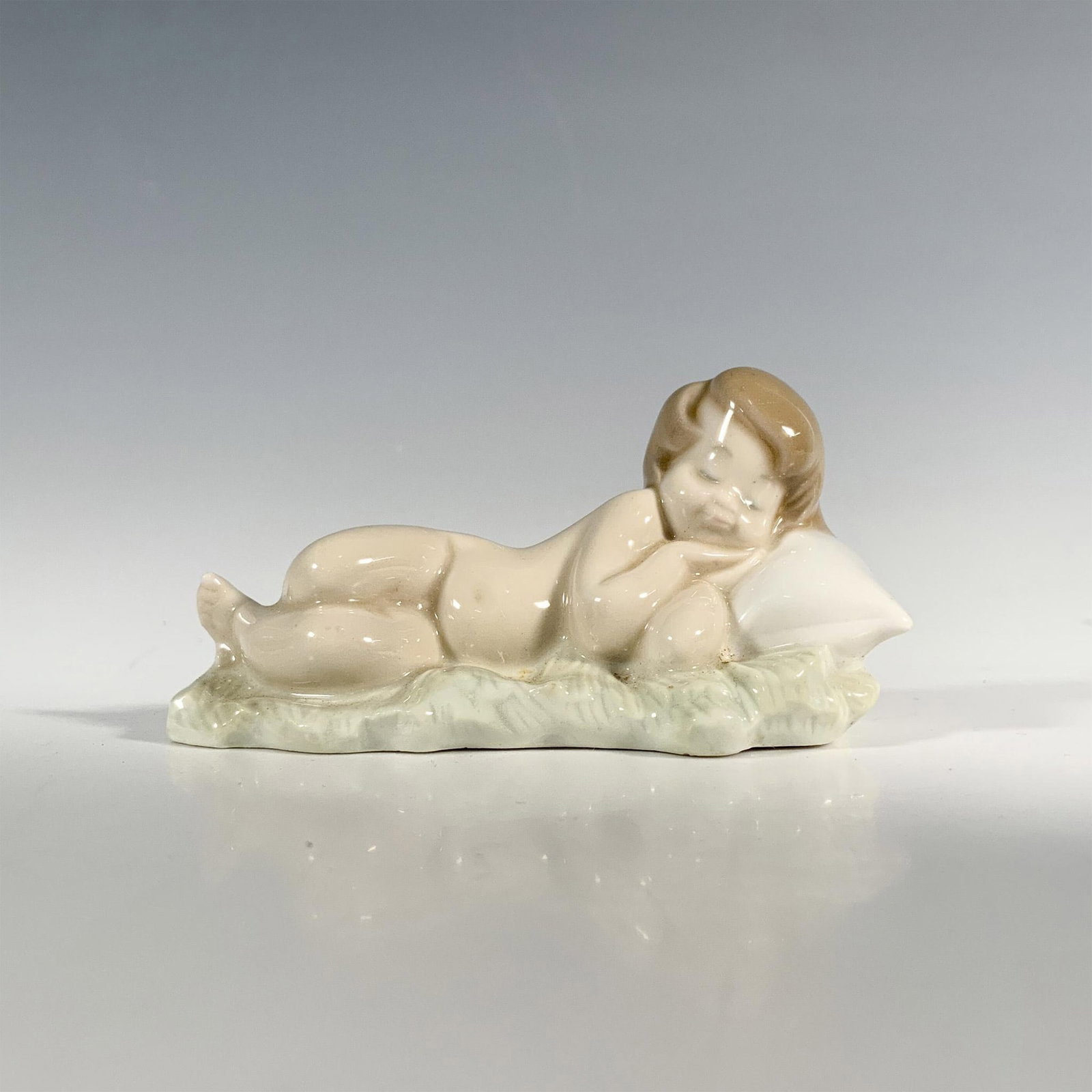 Baby Jesus 1004670 - Lladro Porcelain Figurine: Glossy finish; Lladro backstamp. Artist: Juan Huerta Issued: 1969 - 2001 Dimensions: 2"H x 4"W Manufacturer: Lladro Country of Origin: Spain