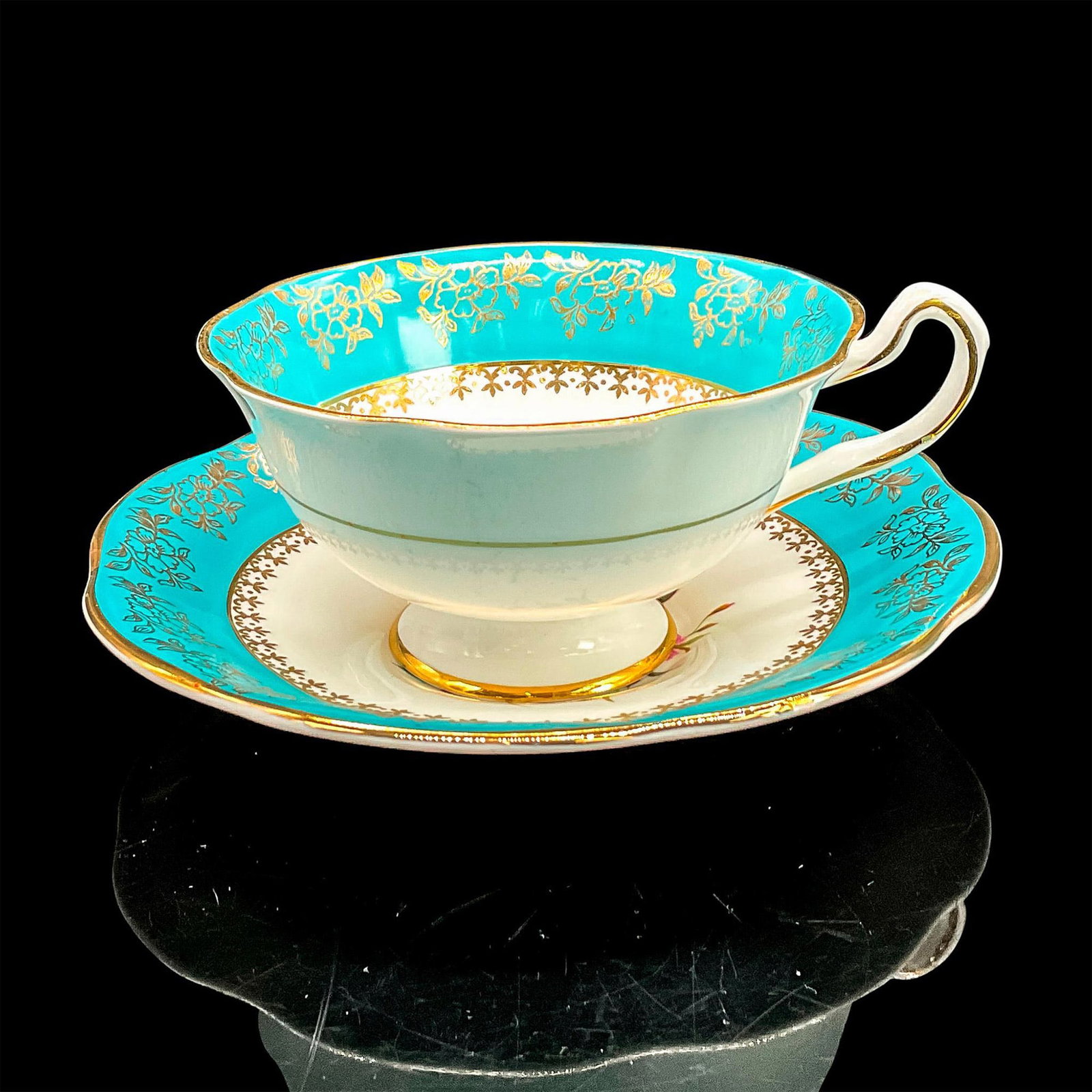 2pc Rosina Bone China Cup + Saucer, Magenta + Pink Roses: Tea cup and saucer with gold floral and leaf design on bright turquoise band, magenta and pink roses, gold rims. Rosina Fine Bone China backstamp. Cup 4.75"L x 4"W x 2.25"H. Saucer 1"H x 5.5" diameter