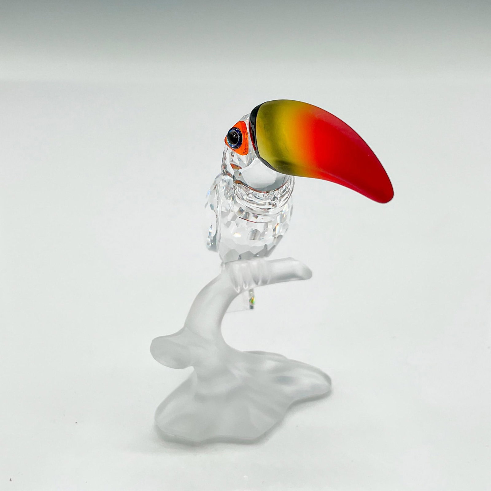 Swarovski Silver Crystal Figurine, Toucan: Part of the Feathered Beauties Collection. Clear faceted body perched on satin crystal branch. Figural has blue crystal eyes with orange crystal accent and large satin red, yellow and black beak. Swar