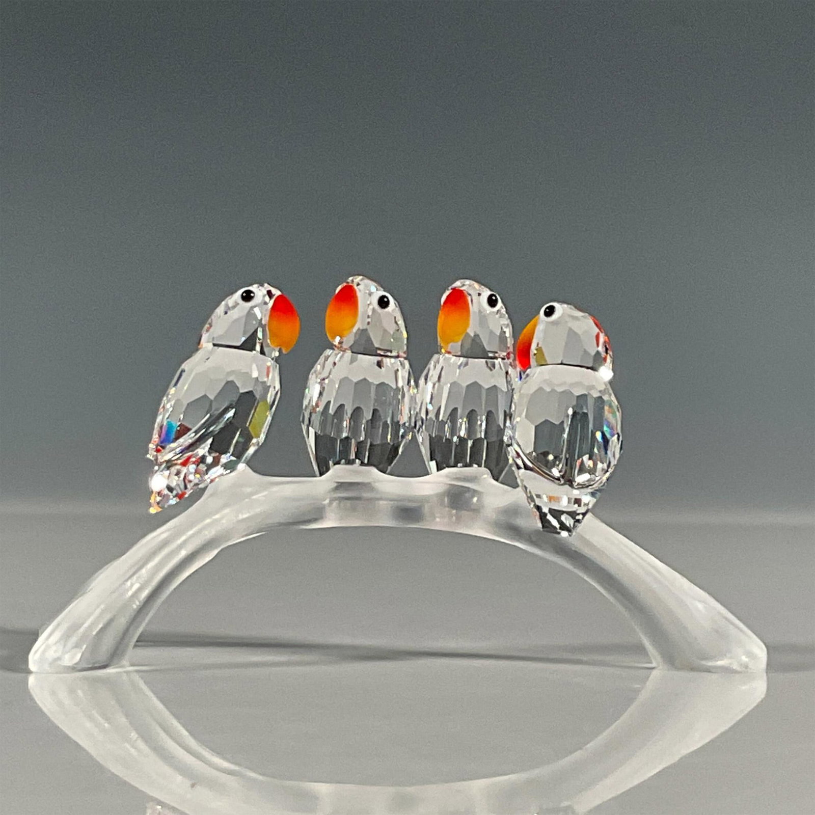 Swarovski Crystal Figurine, Baby Lovebirds: Lead crystal four baby lovebirds sitting on a branch that were part of the Feathered Beauties collection. They sit on a three-pronged arch branch and shine vibrantly with their fire opal beaks. Swarov