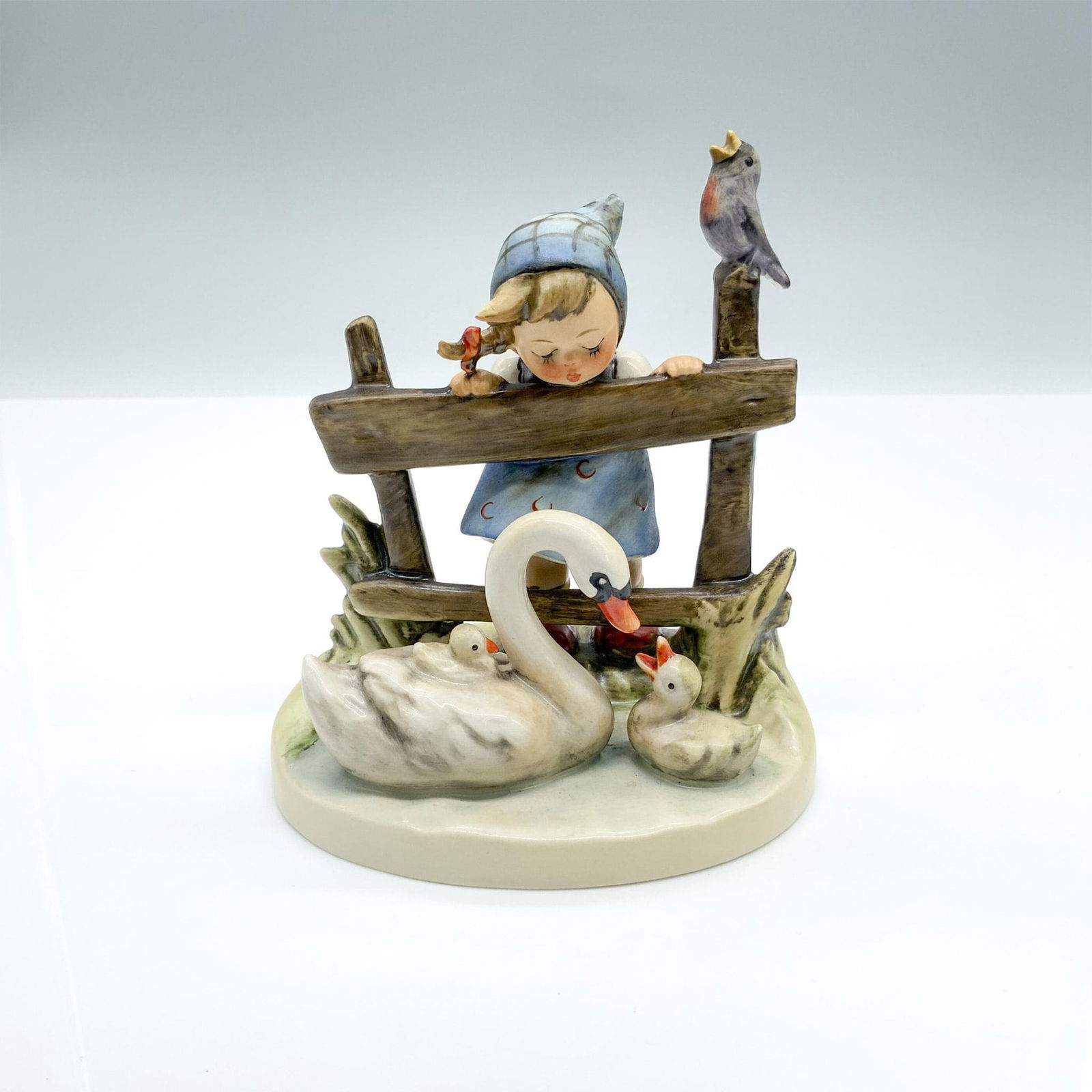 Feathered Friends 344 - Goebel Hummel Figurine: Hand-painted figurine depicting a young girl watching a swan swimming with ducklings while a bird sings on the fence post. Goebel backstamp on the bottom. Dimensions: 4"L x 3.5"W x 4.5"H Manufacturer: