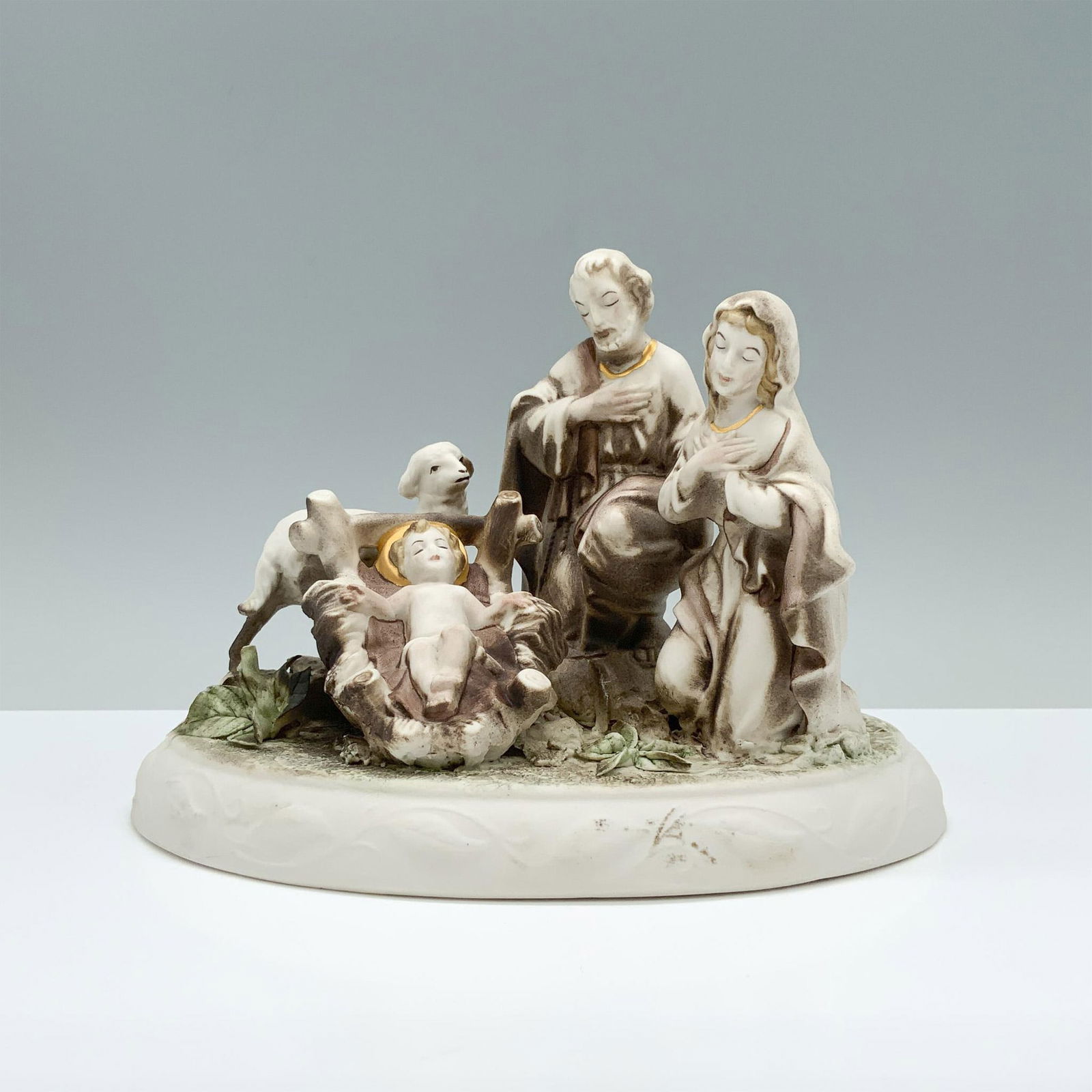 Cybis Porcelain Nativity Figurine, The Holy Family: Depicts Jesus cradled in the manger, watched over by Mary and Joseph in a serene field adorned with rich gold, brown, and green hues. Dimensions: 8"L x 5.5"W x 5.5"H Manufacturer: Cybis Country of Ori