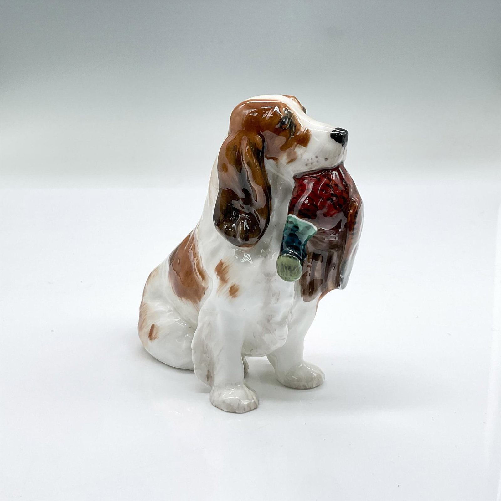 Royal Doulton Dog Figurine, Cocker Spaniel HN1029: Seated small size cocker spaniel with a pheasant in his mouth. Bone china, gloss finish. Royal Doulton backstamp. Issued: 20th century Dimensions: 4.25"L x 1.75"W x 3.75"H Manufacturer: Royal Doulton 