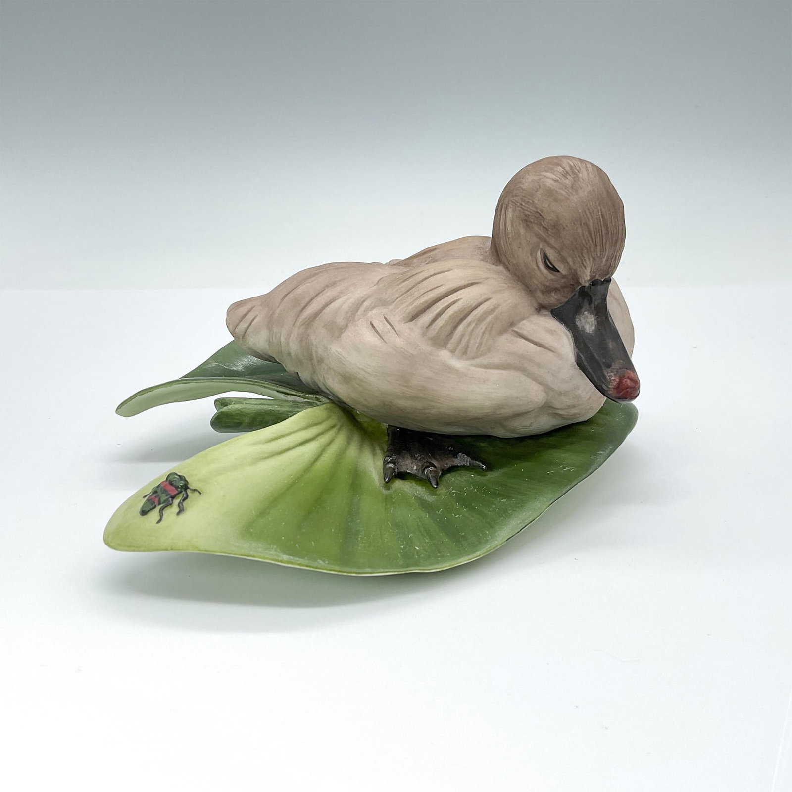 Boehm Cygnet Duck Figurine, Cygnus Olor 400-13: Matte porcelain sculpture featuring a naturalistic depiction of a baby swan resting on a large green lily pad, accompanied by a beetle. Boehm backstamp. Issued: 20th century Dimensions: 6"L x 5"W x 3.