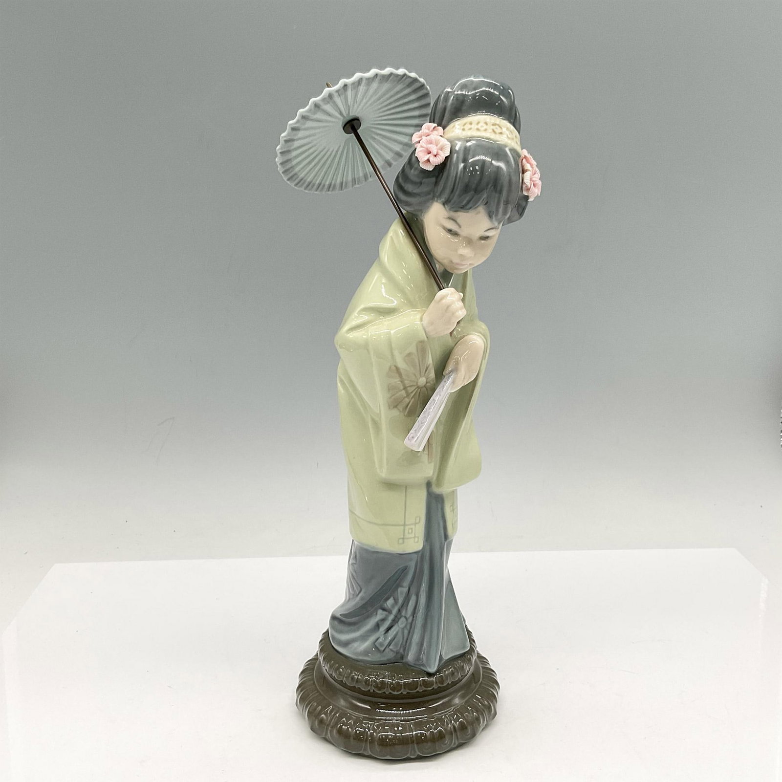 Lladro Porcelain Figurine, Oriental Spring 1004988: Glossy young Japanese figural dressed in green kimono with blue dress holding her umbrella and fan. Lladro backstamp. Artist: Salvador Debon Issued: 1978 - 1996 Dimensions: 11.25"H x 3.75" dia. Manufa