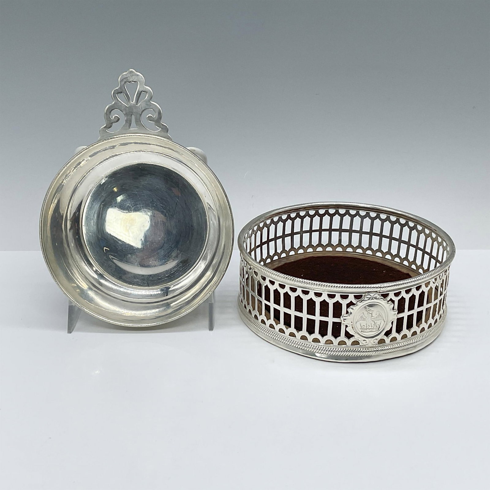 2pc Vintage Sterling Silver Wine Coaster and Tasting Cup: Exquisite, reticulated silver-sided coaster featuring an emblem badge and a turned walnut base. Also, a reticulated decorative handled silver tastevin with a rolled edge. Total weight: 160 grams. Coas