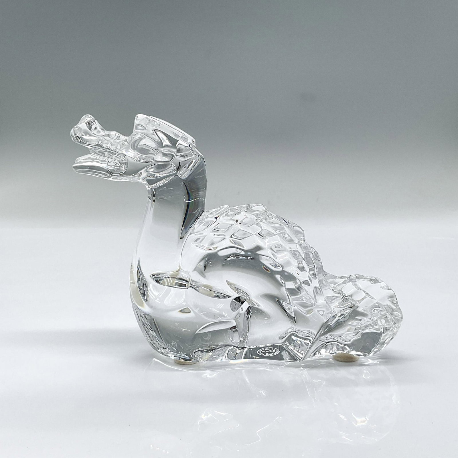 Baccarat Crystal Figurine, Dragon: Striking clear crystal figure of a seated dragon looking upwards. Baccarat mark. Issued: 20th century Dimensions: 5.25"L x 1.5"W x 3.75"H Manufacturer: Baccarat Country of Origin: France