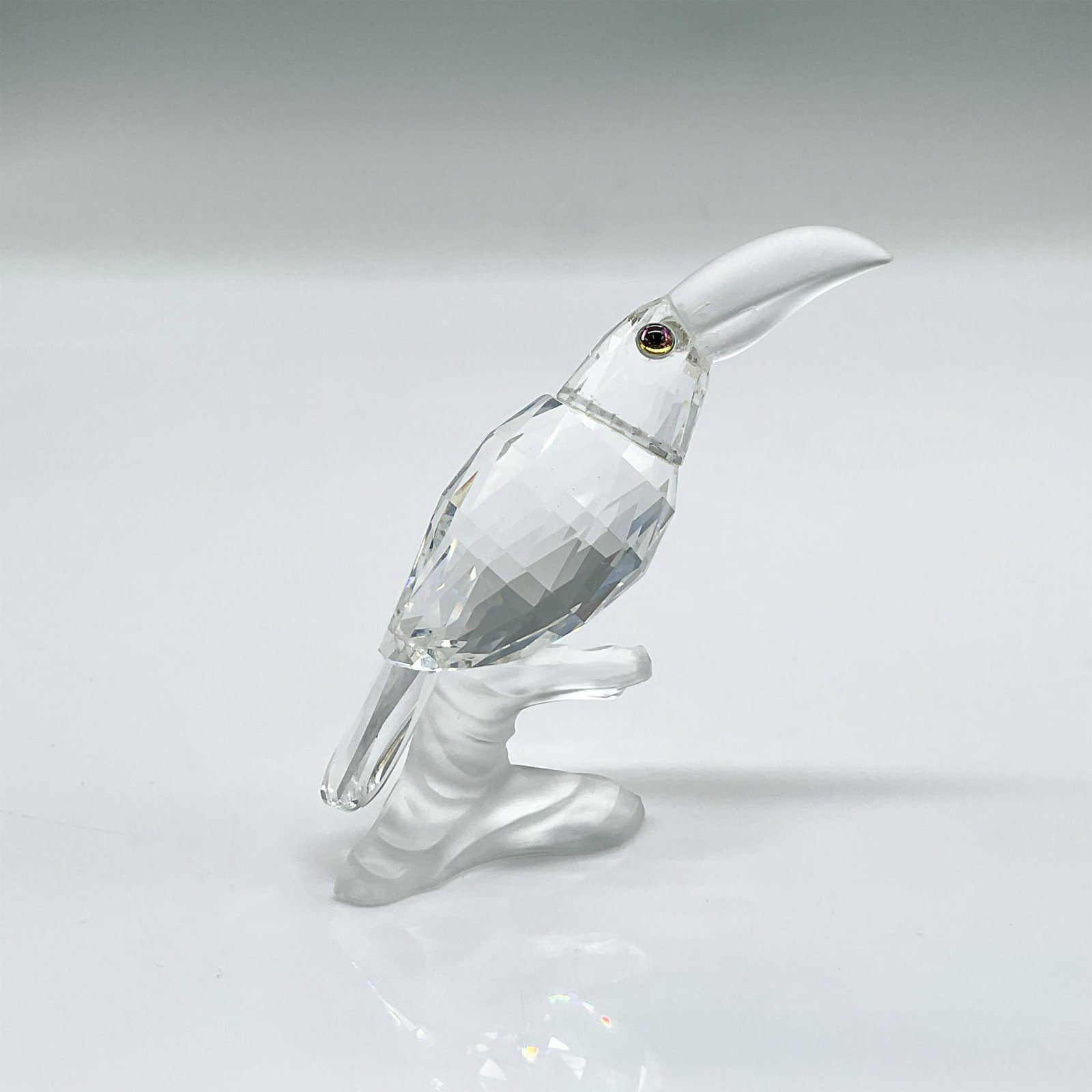 Swarovski Silver Crystal Figurine, Toucan: Clear faceted crystal figure of a toucan with blue/green/pink eyes frosted beak, perched on a frosted crystal base. Part of the Up in the Trees collection. Swarovski mark. Issued: 1989-1992 Dimensions