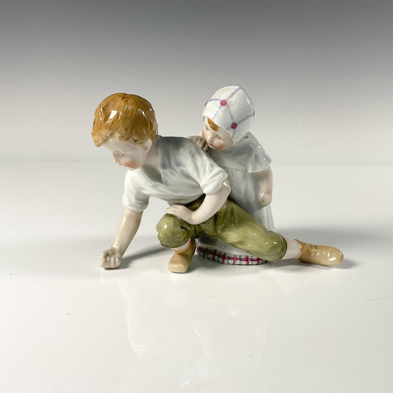 Porcelain Figurine, Playing Marbles: Hand painted boy in green pants playing marbles, with a young girl overlooking his shoulder. Issued: 20th century Dimensions: 6.5"L x 3.5"W x 4.5"H