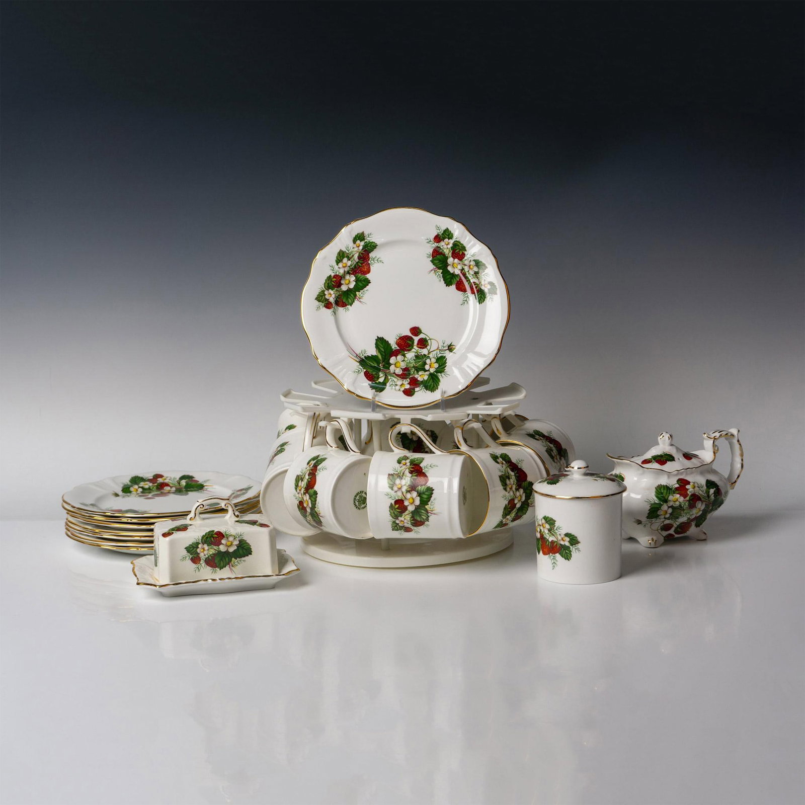 20pc Hammersley Bone China Tea Service, Strawberry Ripe: Lovely strawberry pattern throughout with gilt accents on rim and handles. Lot includes tea pot 8", jam jar 4.5", butter dish 6", 8 cups, 8 breakfast plates 8" and cup hanger rack. Hammersley backstam