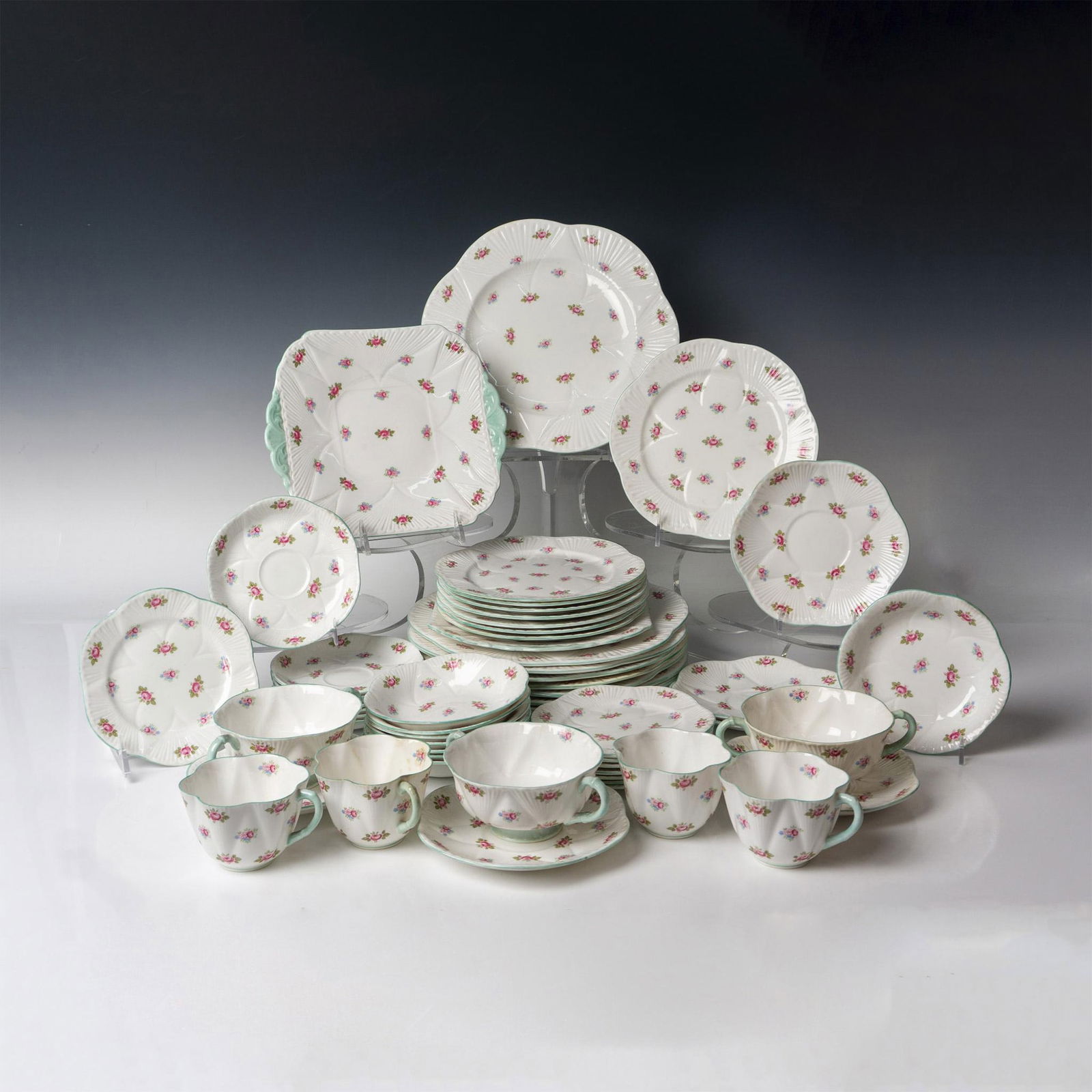 54pc Shelley Bone China Serv. for 8 Dinnerware, Rosebud: Decorated with delicate roses surrounded by green leaves. Rims are colored green. Service is a incomplete set but includes 8 - Dinner plates 11", 2 - square sandwich plates 9.5", 8 - salad plates 8",