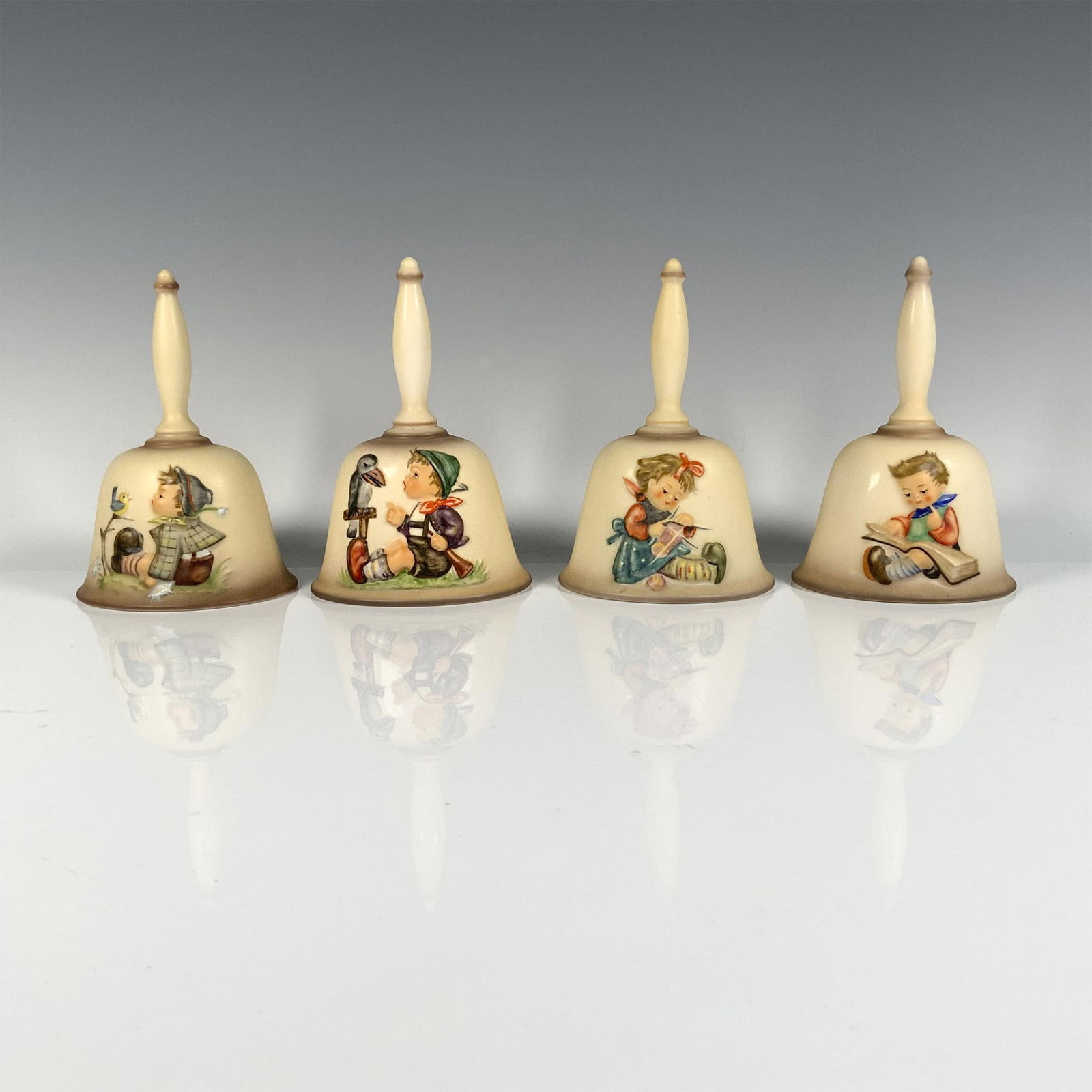 4pc Goebel Hummel Annual Bells, HUM 702, 705, 708, 714: In this delightful set you'll find scenes of a boy reading a book (1980), a girl sewing (1983), a young boy with his pet parrot (1986), and a young boy with his pet canary (1992). Goebel Hummel backst