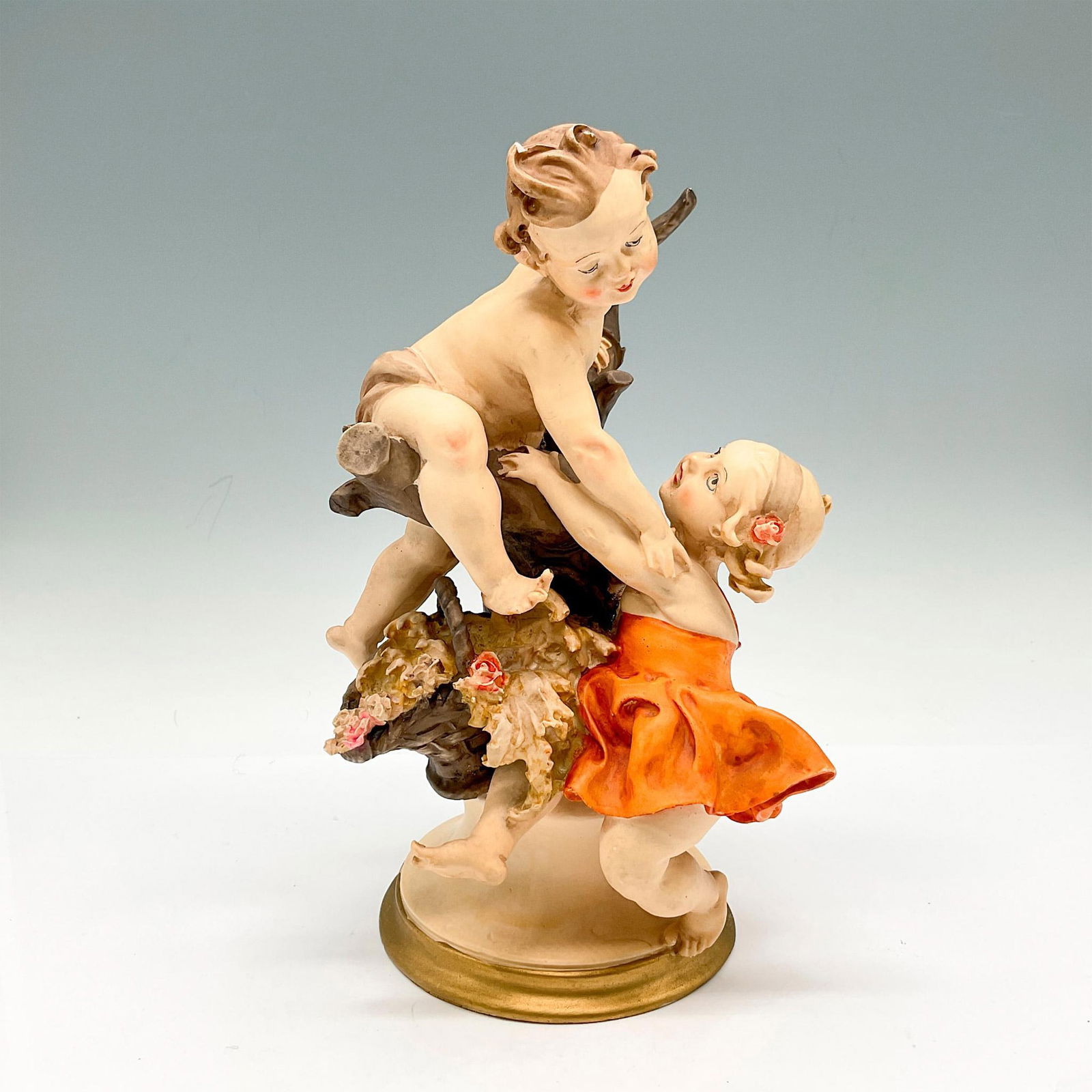 Vintage Capodimonte Style Children at Play Figurine: Matte finished figure on pedestal base. Colored in browns, orange and pink. Solid base with gold toned band. Issued: 20th century Dimensions: 5"L x 6"W x 9"H
