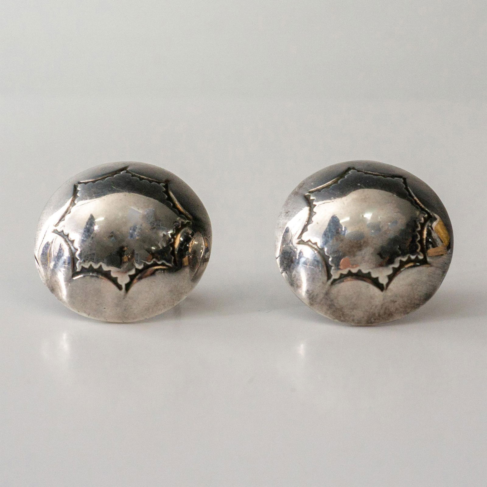 Native American Round Sterling Silver Screw-Back Earrings: Screw-back earrings featuring a round dome shape with an etched tribal design. Sterling impressed mark. 10 grams. Issued: 20th century Dimensions: 21mm dia.