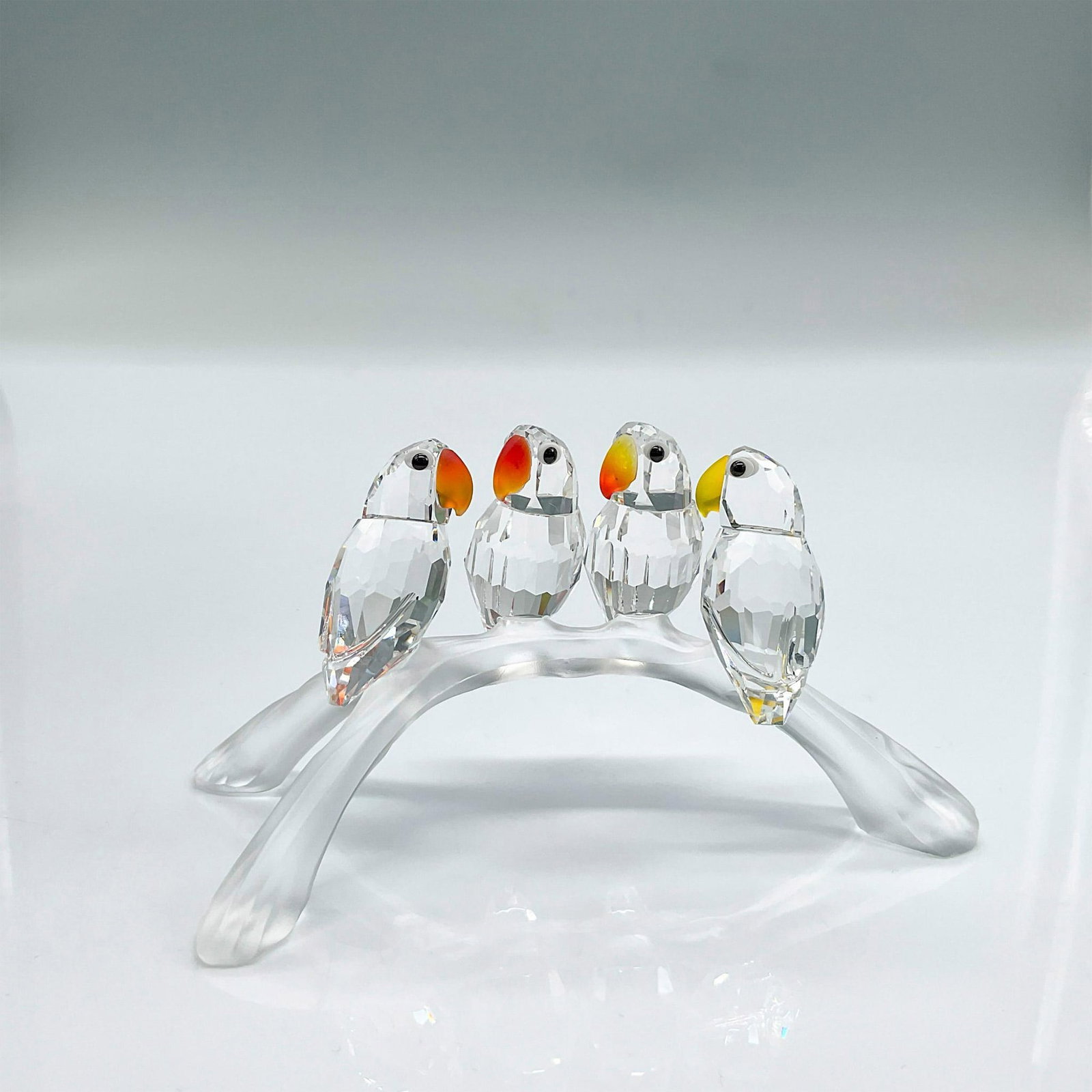 Swarovski Crystal Figurine, Baby Lovebirds: Four clear faceted crystal birds perched on a satin crystal branch. They have bright red/orange/yellow beaks and black eyes. Swarovski mark. Includes original box: 5"H x 6" dia. Issued: 1996-2011 Dime