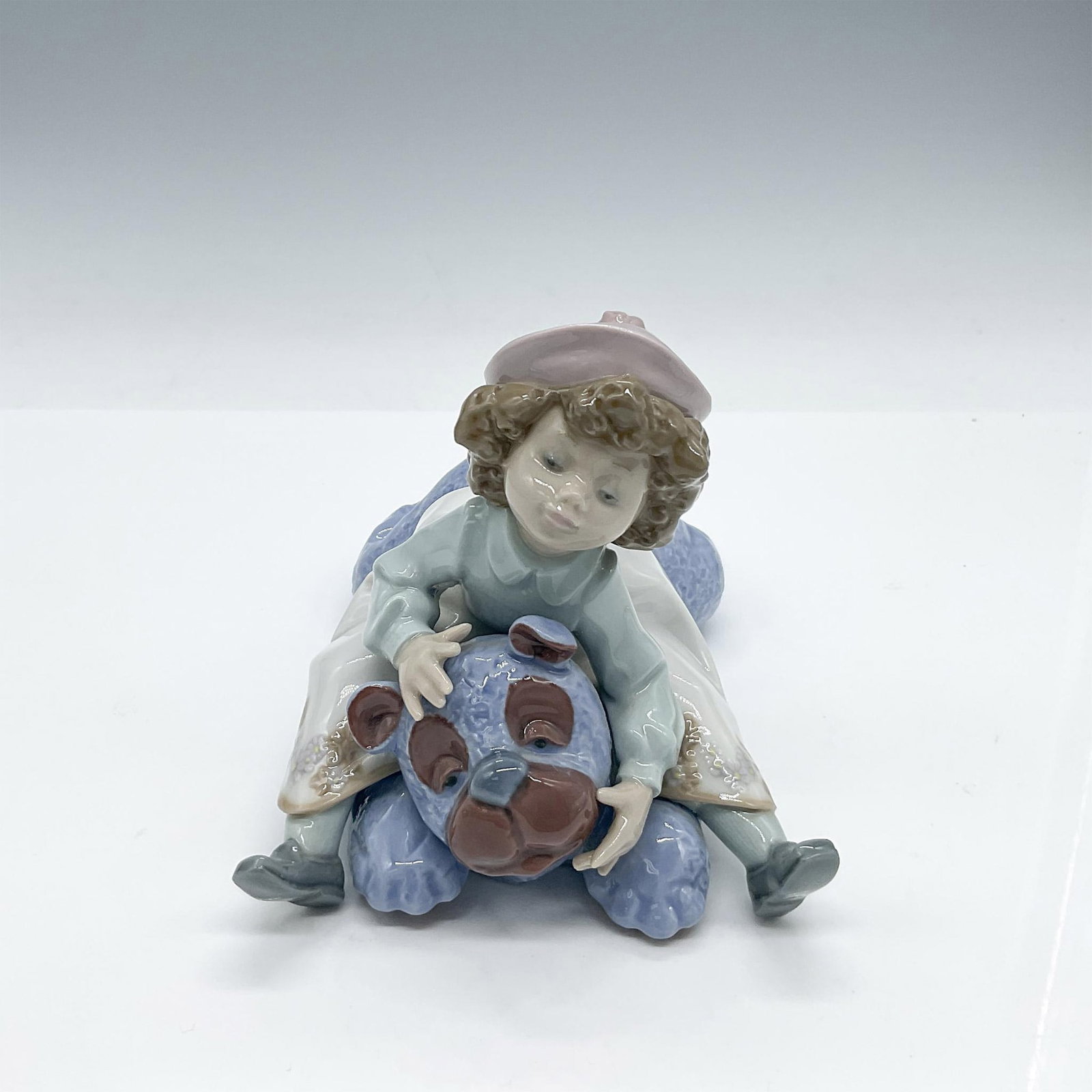 Lladro Porcelain Figurine, Giddy Up 1005664: Glossy figure of an adorable young girl playing on her large fluffy blue stuffed animal. She is wearing a lovely frock and a pretty pink beret. Lladro backstamp. Artist: Francisco Polope Issued: 1990-