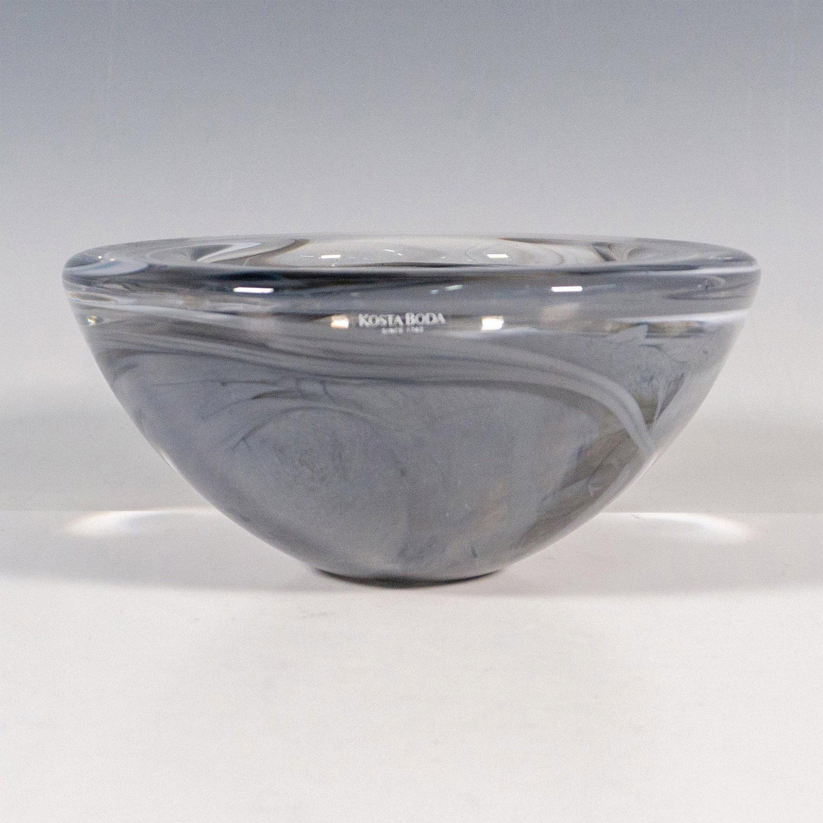 Kosta Boda by Anna Ehrner Glass Bowl, Atoll: A round clear glass decorative bowl with gray swirls. Kosta Boda stickered. Artist: Anna Ehrner Dimensions: 7"W x 3.25"H Manufacturer: Kosta Boda Country of Origin: Sweden