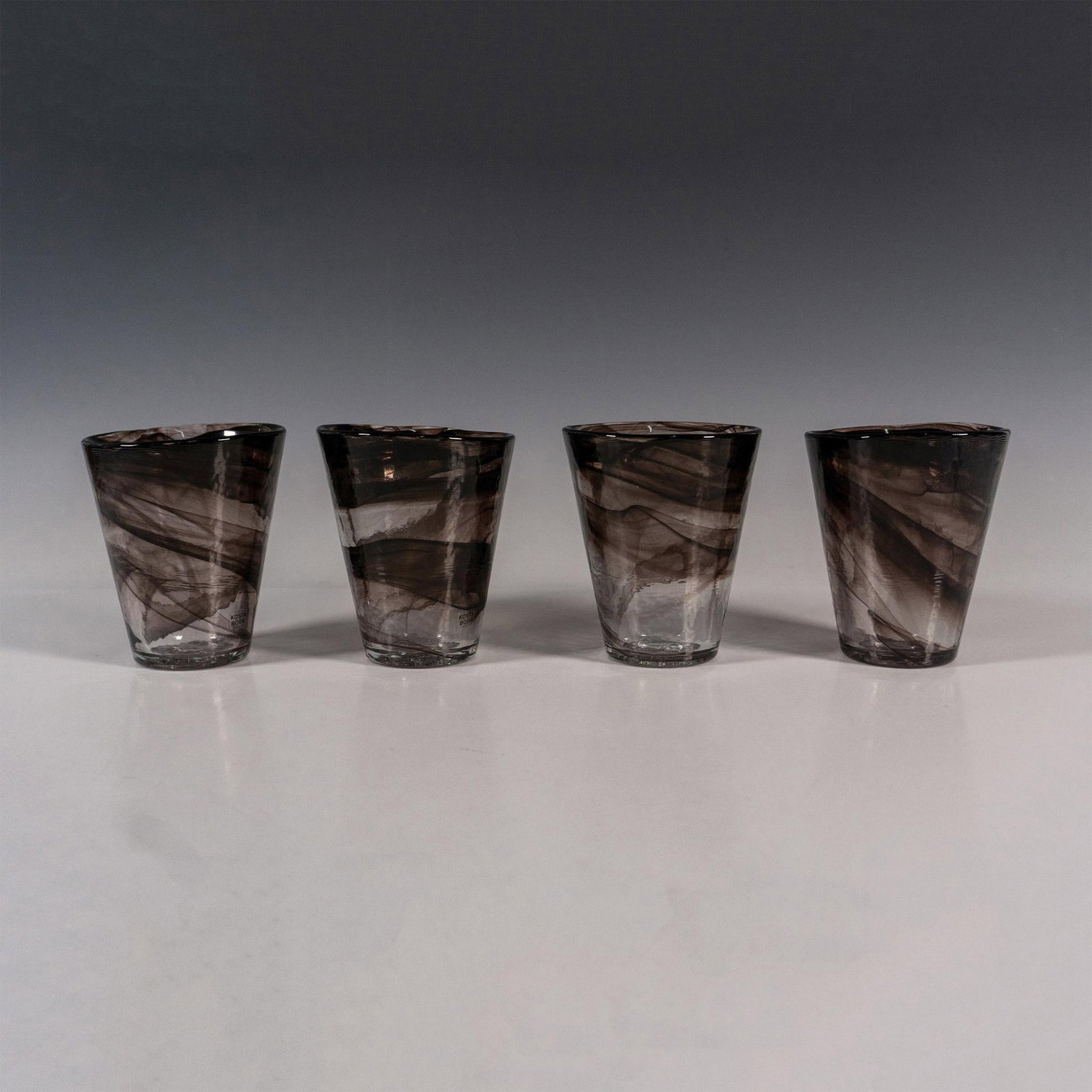 4pc Kosta Boda by Ulrica Hydman-Vallien Glass Tumblers, Mine: A set of 4 glassware. Clear with glass swirls. Kosta Boda stickered on the rim. Artist initials on the underside. This item has its original box: 4.25"L x 4.25"W x 5.25"H. Artist: Ulrica Hydman-Vallie