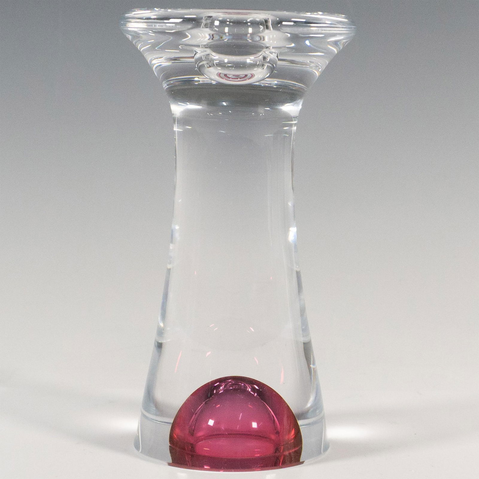 Kosta Boda by Goran Warff Glass Candlestick Holder, Zoom: A clear abstract form candle holder accented with a magenta-pink glass bubble at the bottom. Kosta Boda and artist's name etched on the underside. This item has its original box: 4.25"L x 4.25"W x 7.5