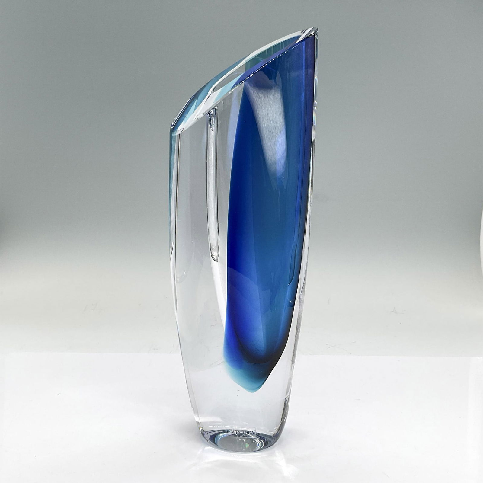 Kosta Boda Glass Vase, Saraband Blue: Striking vase in clear and blue glass. It is a sculpture, a vase, and an art piece all in one. Kosta Boda affixed label. Artist: Goran Warff Dimensions: 4.25"L x 2"W x 11"H Manufacturer: Kosta Boda Co