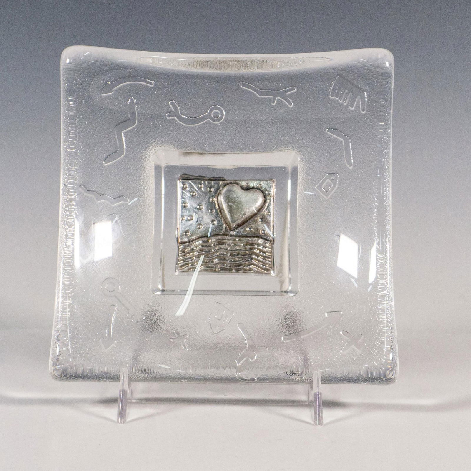 Kosta Boda by Bertil Vallien Domino Glass Bowl: Part of the Domino collection designed by Bertil Vallien (Sweden, b. 1938). A jewelry bowl with a clear surface and a satin underside. Features various debossed abstract symbols, and in silver-color a