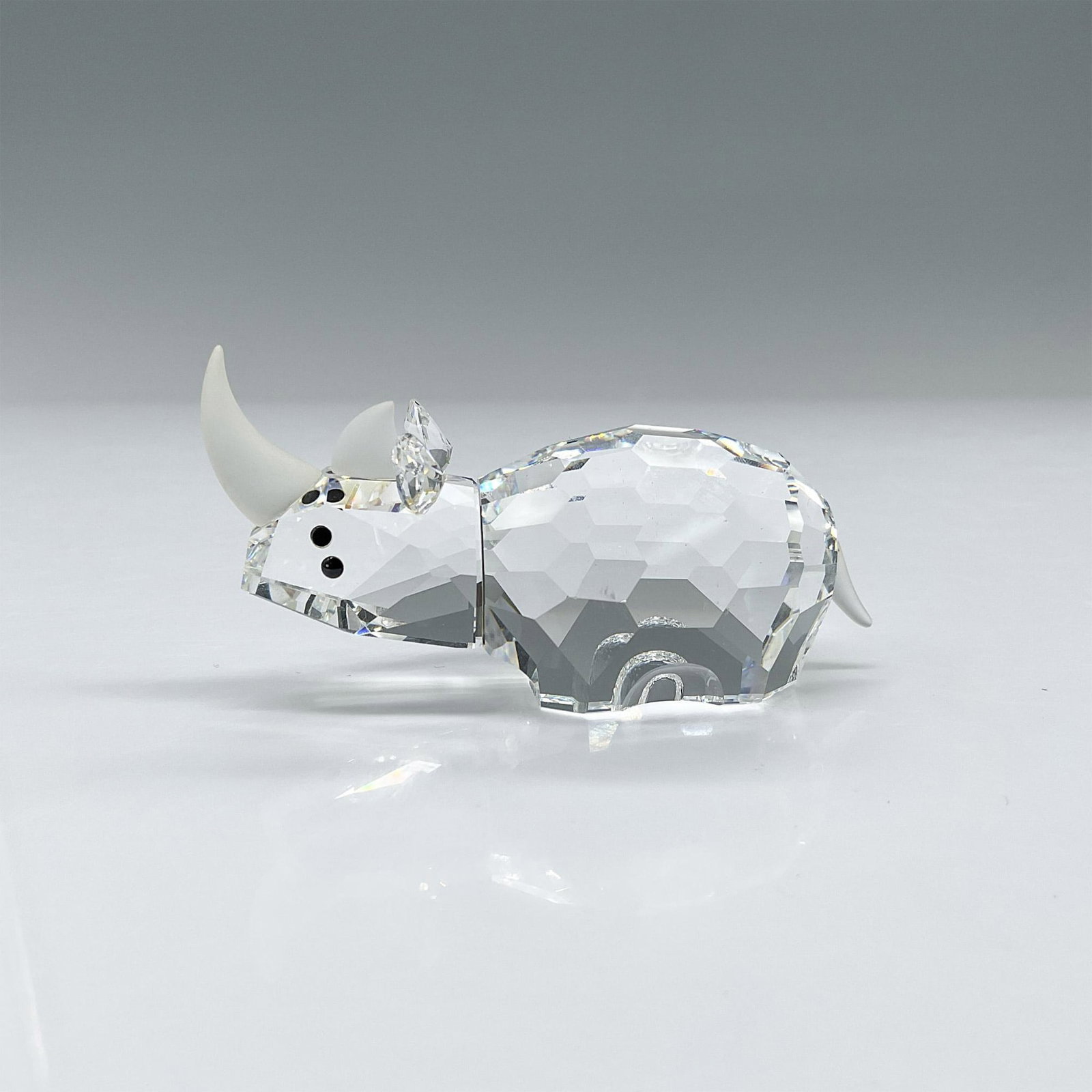 Swarovski Crystal Figurine, Rhinoceros: Clear crystal rhino figurine with black eyes and frosted horns and tail, part of the African Wildlife theme group. This item has its original box which measures 5.25"H x 3.5" dia. Artist: Adi Stocker 
