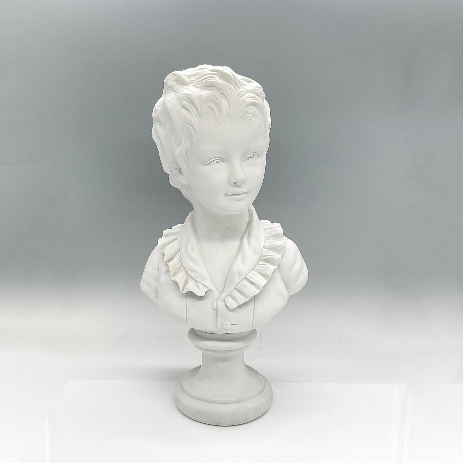 Capodimonte Bust, L'Enfant Brongniart: Matte white porcelain bust of a young boy. Capodimonte mark. Engraved on the back: A. Brongniart enfant, apres Houdon. Dimensions: 8.25"L x 6.5"W x 16"H Manufacturer: Capodimonte Country of Origin: It