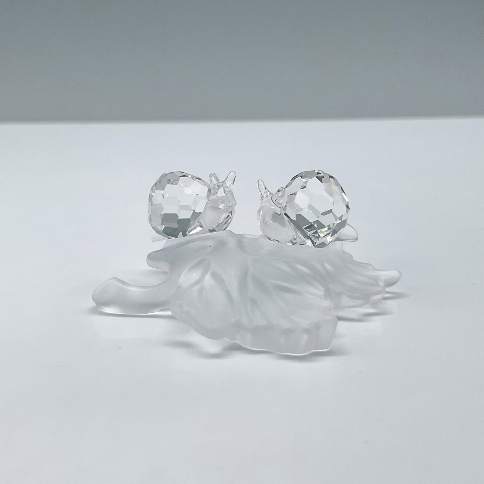 Swarovski Crystal Figurine, Baby Snails On Leaf: Clear crystal snail duo sitting on a frosted crystal leaf. Includes certificate and the original box, dimensions: 3.25''H x 3.25''dia. Swarovski etched backstamp. Issued: 20th century Dimensions: 2''L