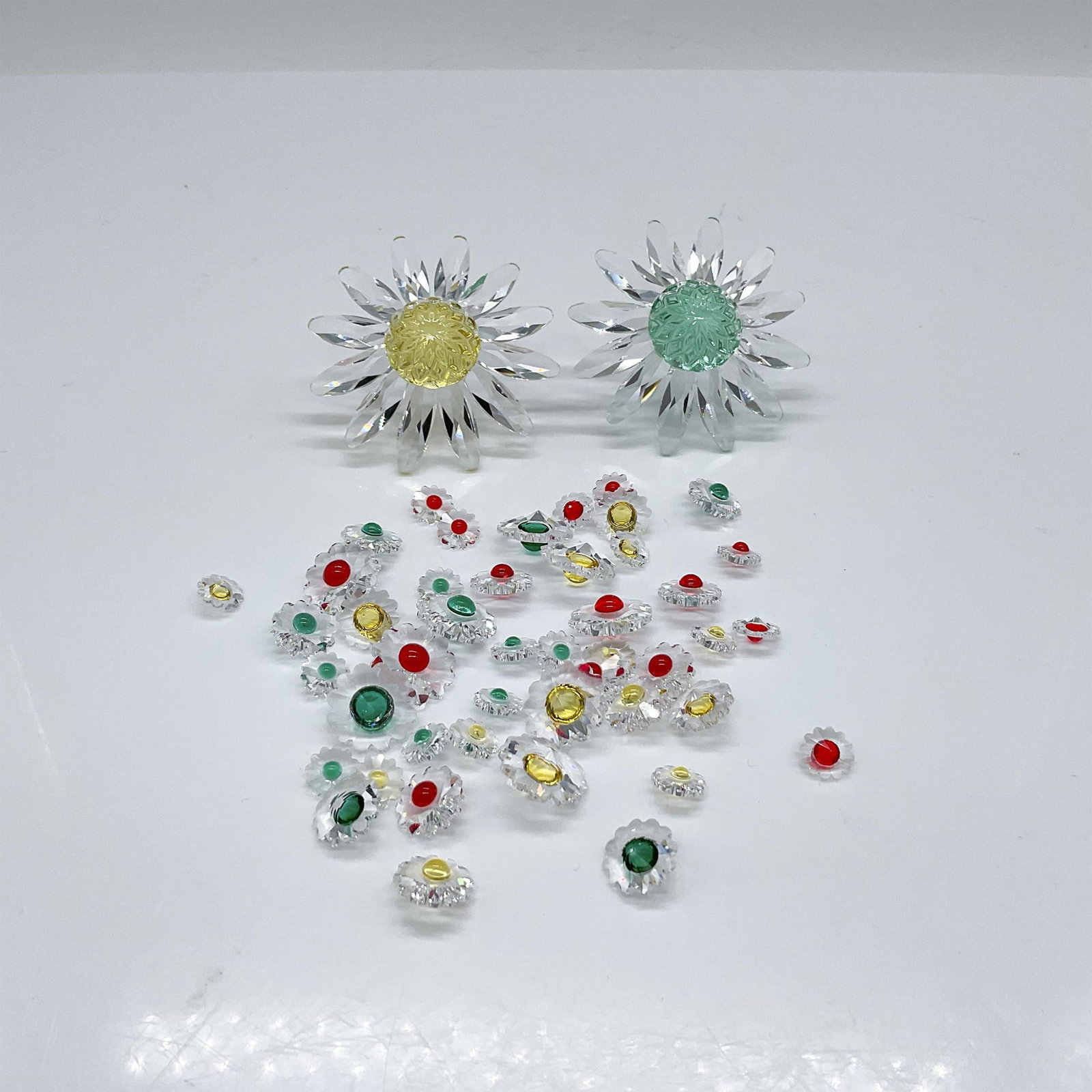 47pc Swarovski Crystal Marguerite Figurines & Paperweights: Part of the renewal gift. Includes the 1999 yellow flower, the 2001 green flower, and 45 mini yellow, green and red flowers. Swarovski marked. The largest piece measures: 2"L x 1.5"W x 1.25"H. Issued: