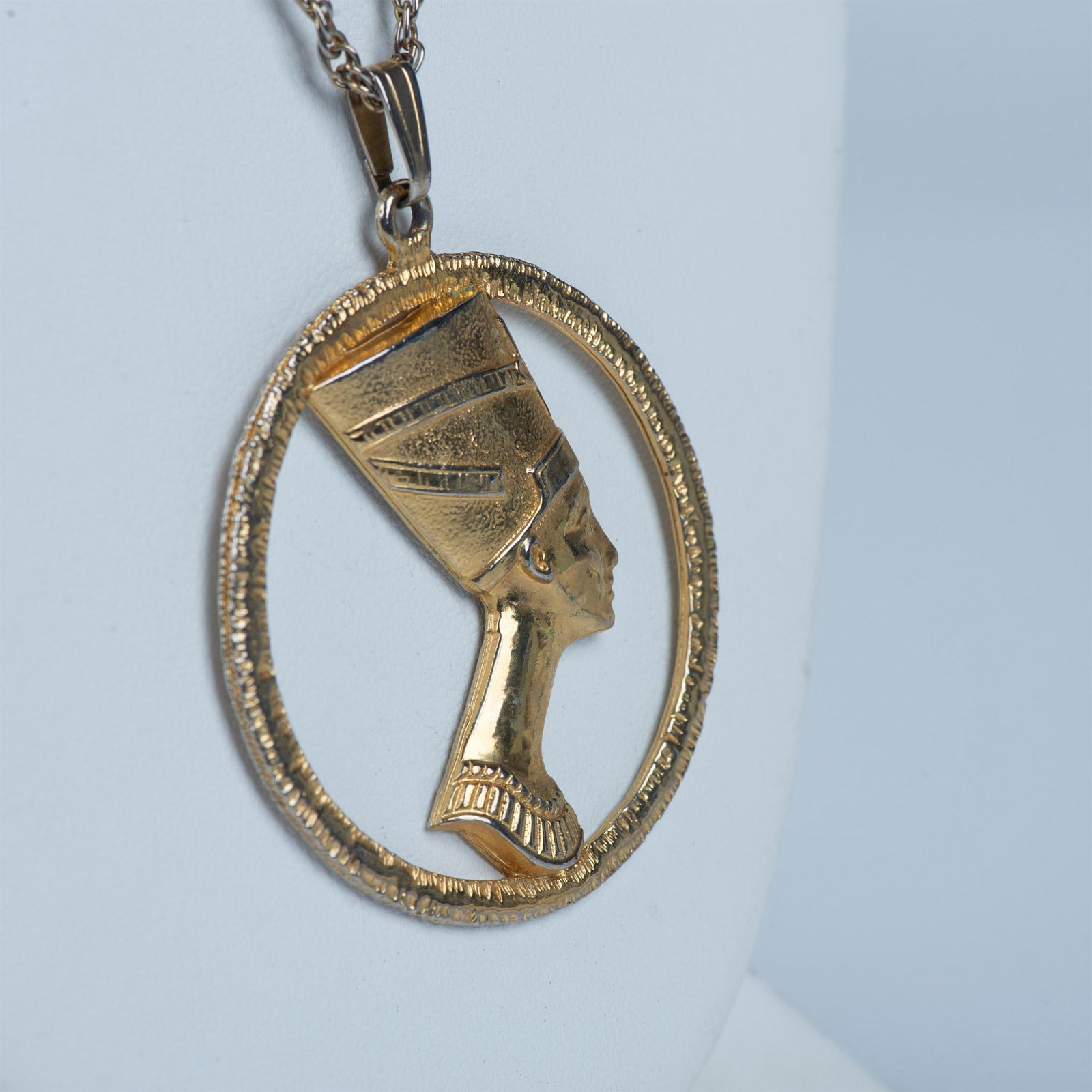 Egyptian Queen Nefertiti Pendant Necklace: This goldtone necklace has a round pendant depicting the ancient Egyptian Queen Nefertiti that measures approximately 2.5"L x 2"W. The chain measures 24.75"L.
