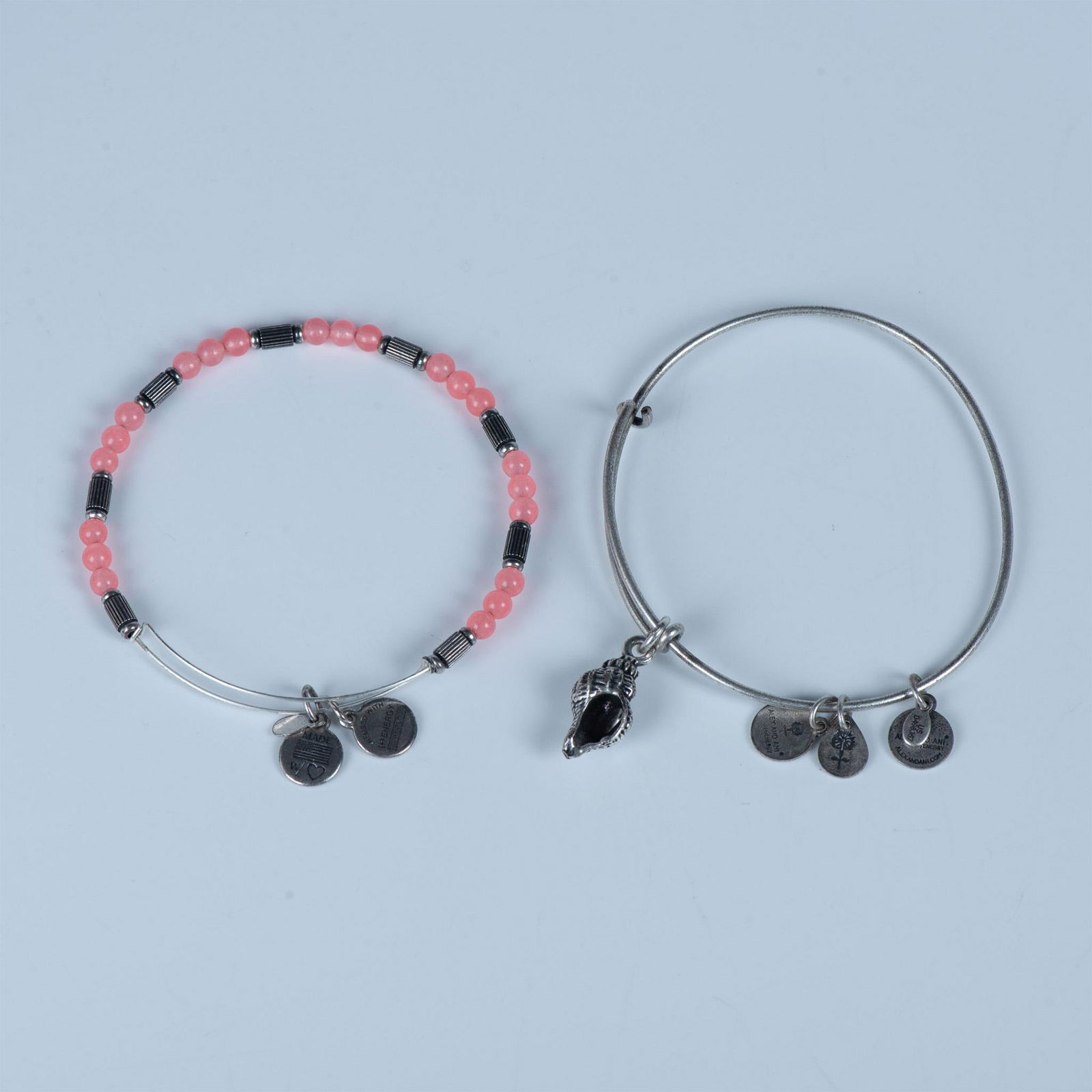 2pc Alex and Ani Positive Energy Bracelets: Two bangle charm bracelets. The first has round pink beads and the second has a seashell charm. They measure approximately 2.5"dia. Manufacturer: Alex and Ani Jewelry Country of Origin: United States