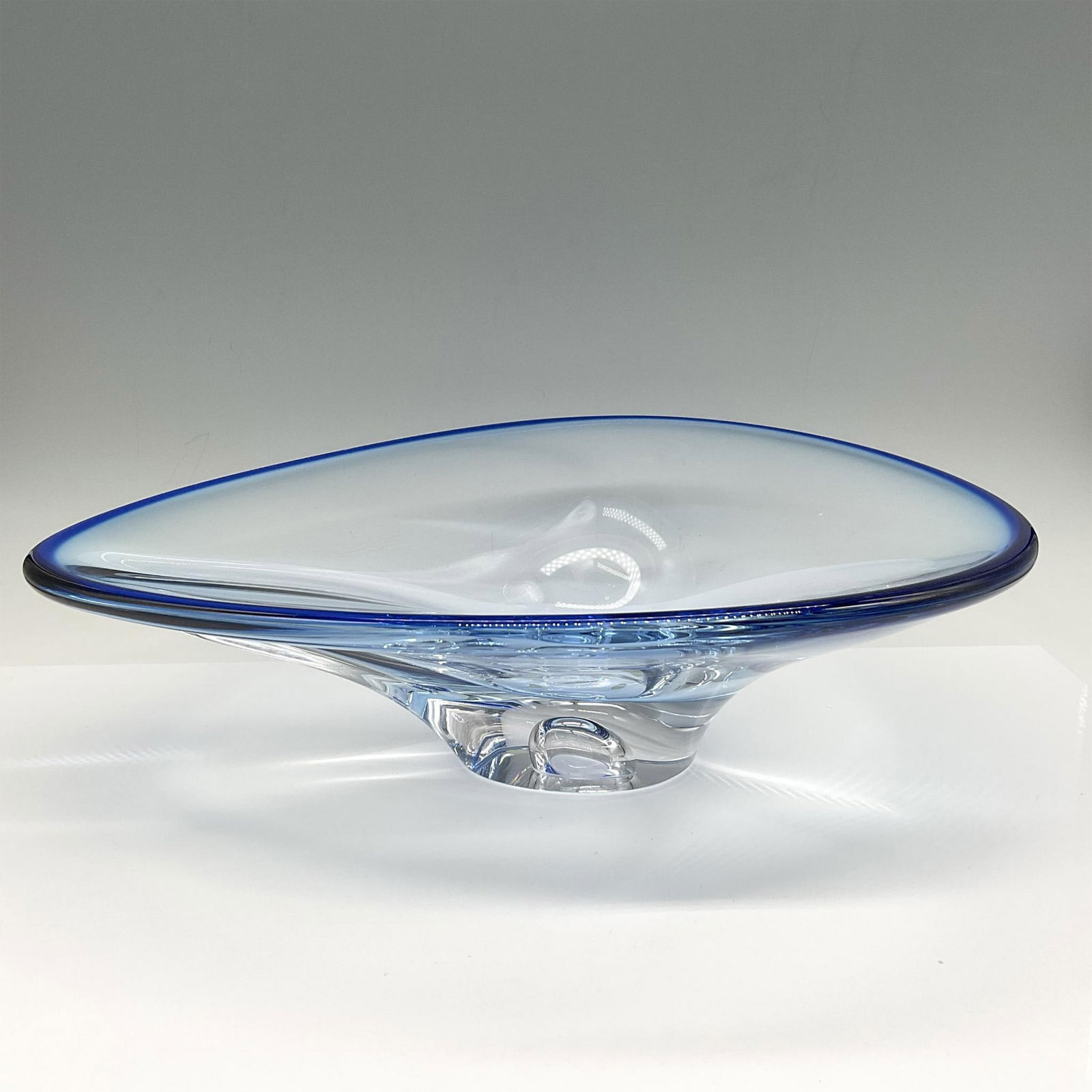 Goran Warff for Kosta Boda Blue Oval Centerpiece Bowl: Blue sculpted glass tapered with clear glass base. Signed by artist. Kosta Boda mark. Artist: Goran Warff Issued: 21st century Dimensions: 12"L x 10"W x 3.5"H Manufacturer: Kosta Boda Country of Orig