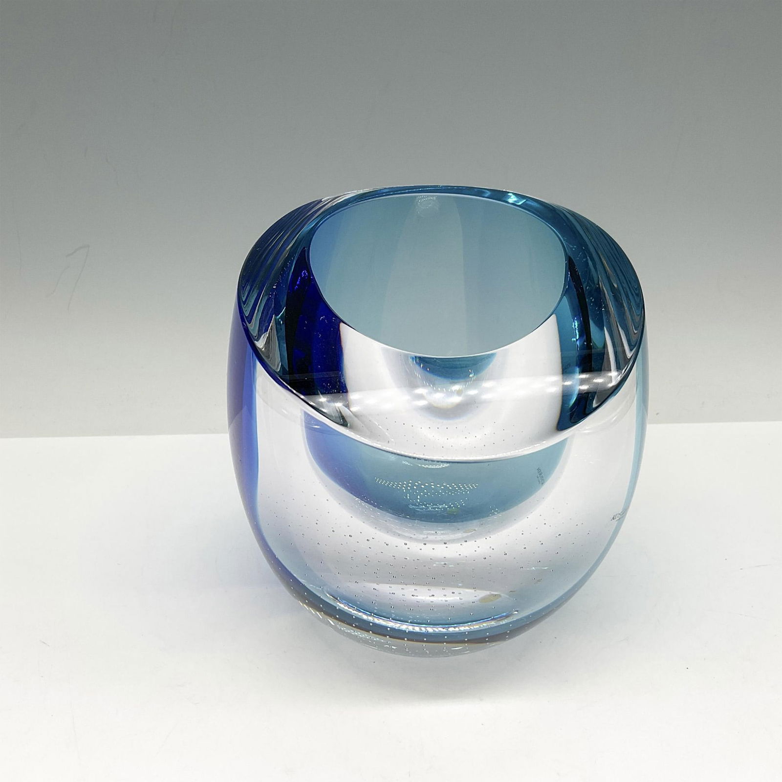 Kosta Boda Blue Glass Bowl: Alluring design of clear and cobalt blue glass merged. Signed by artist. Kosta Boda sticker. Artist: Goran Warff Issued: 1964 - 2022 Dimensions: 4.5"L x 5.5"W x 5"H Manufacturer: Kosta Boda Country o