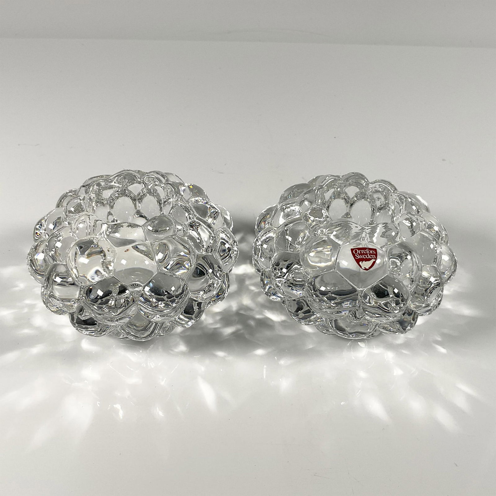 2pc Orrefors Crystal Candleholder, Hallon Raspberry Votive: Duo of Thick clear crystal in the raspberry pattern from the Hallon series. Orrefors etched backstamp. Artist: Anne Nilsson Dimensions: 3''H x 4''dia, Each. Manufacturer: Waterford Country of Origin: