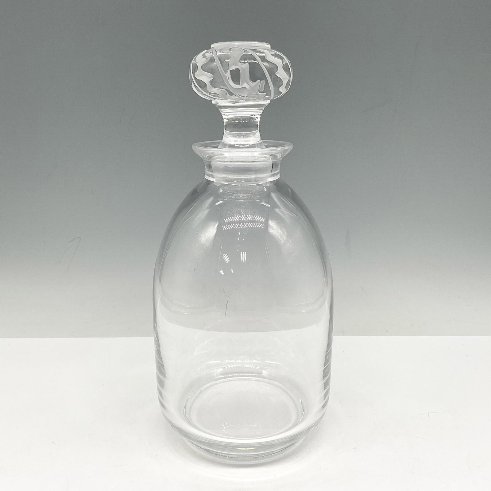 Lalique Crystal Decanter with Stopper: Clear elegant shape with fluted edger. Crystal stopper has cut design. Lalique France etched mark. Issued: 20th century Dimensions: 9.5"H x 4.5" dia. Manufacturer: Lalique Country of Origin: France