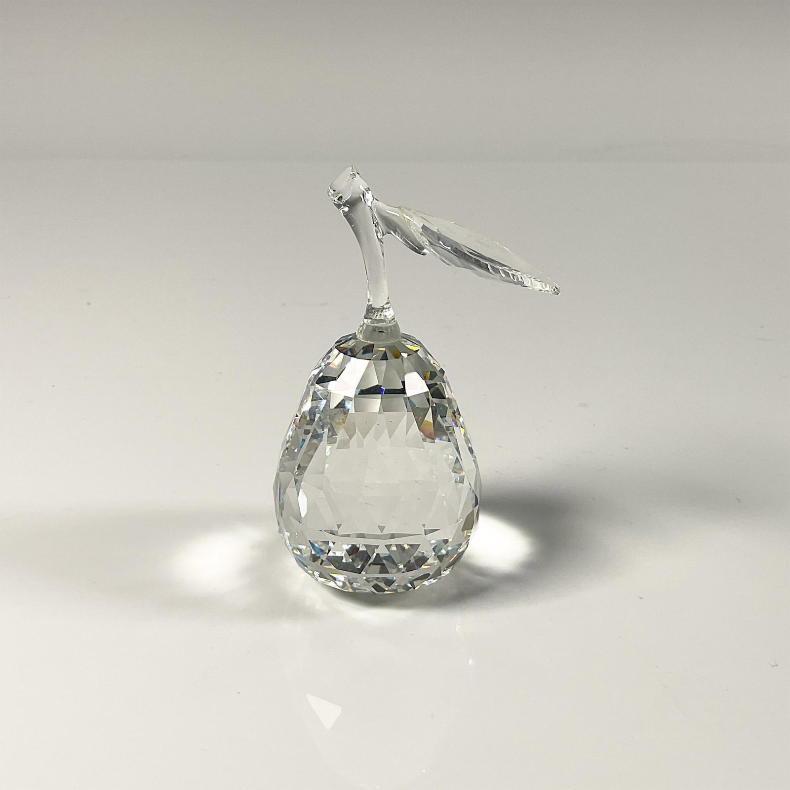 Swarovski Crystal Figurine, Pear: Dazzling facetted clear crystal, depicts a pear with a leaf. Swarovski etched backstamp. Includes the original box, dimensions: 5''H x 6''dia. Dimensions: 3.5''H x 1.75''dia Manufacturer: Swarovski Co